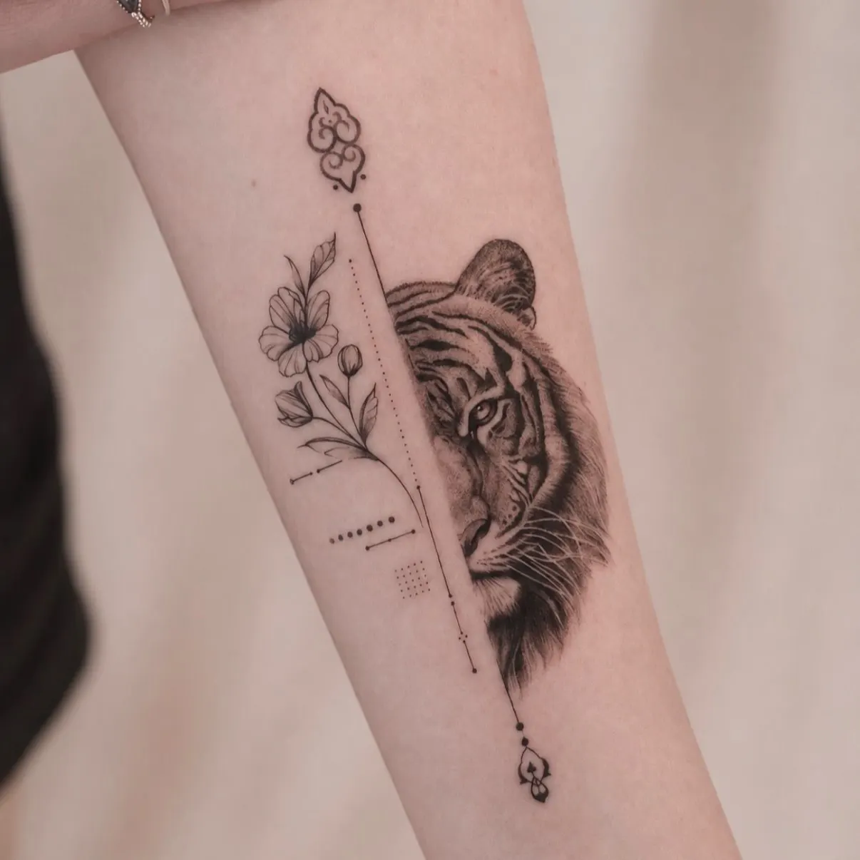 Forearm tattoo of half a tiger face beside fine-line flowers and dotted lines.