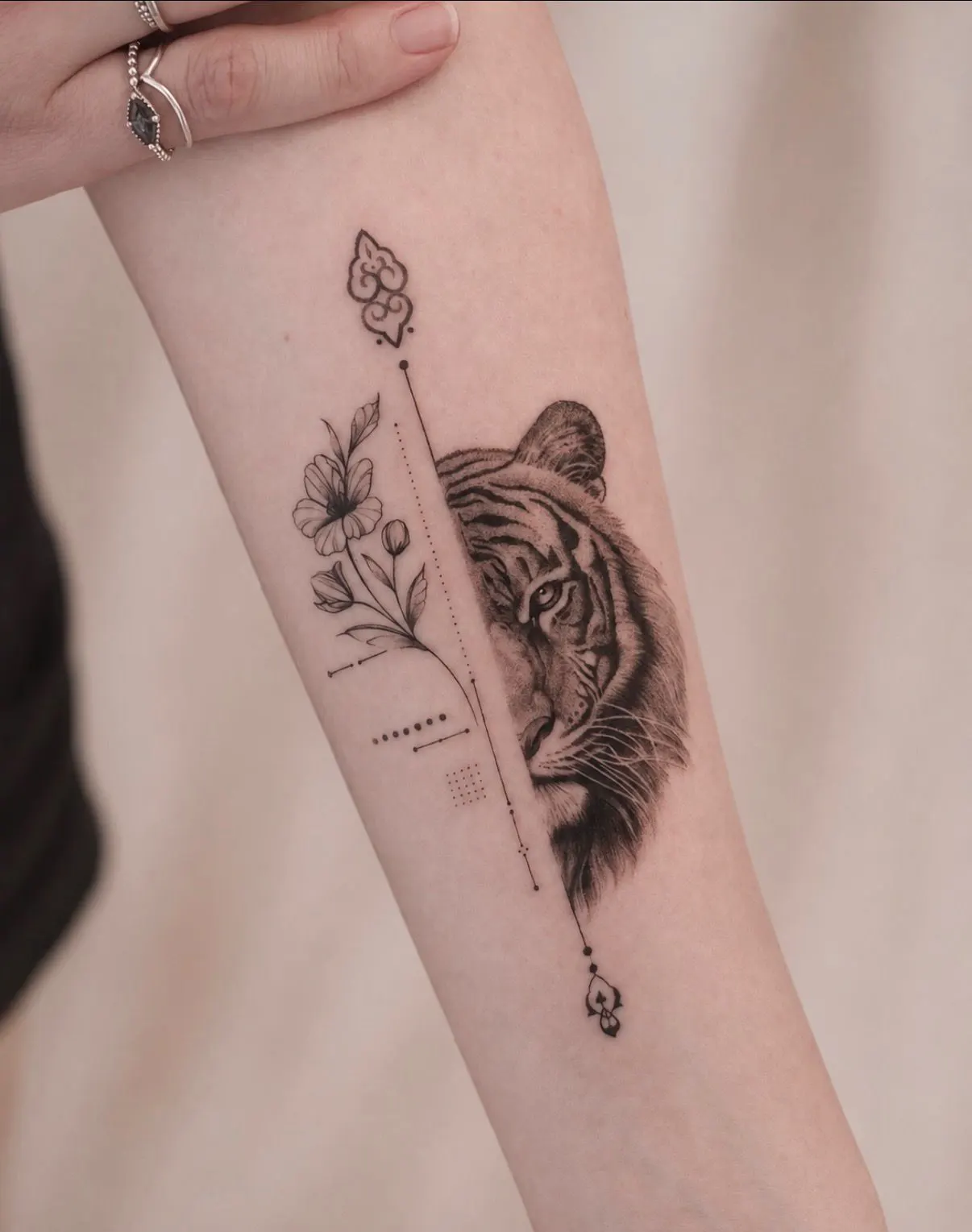 Forearm tattoo of half a tiger face beside fine-line flowers and dotted lines.