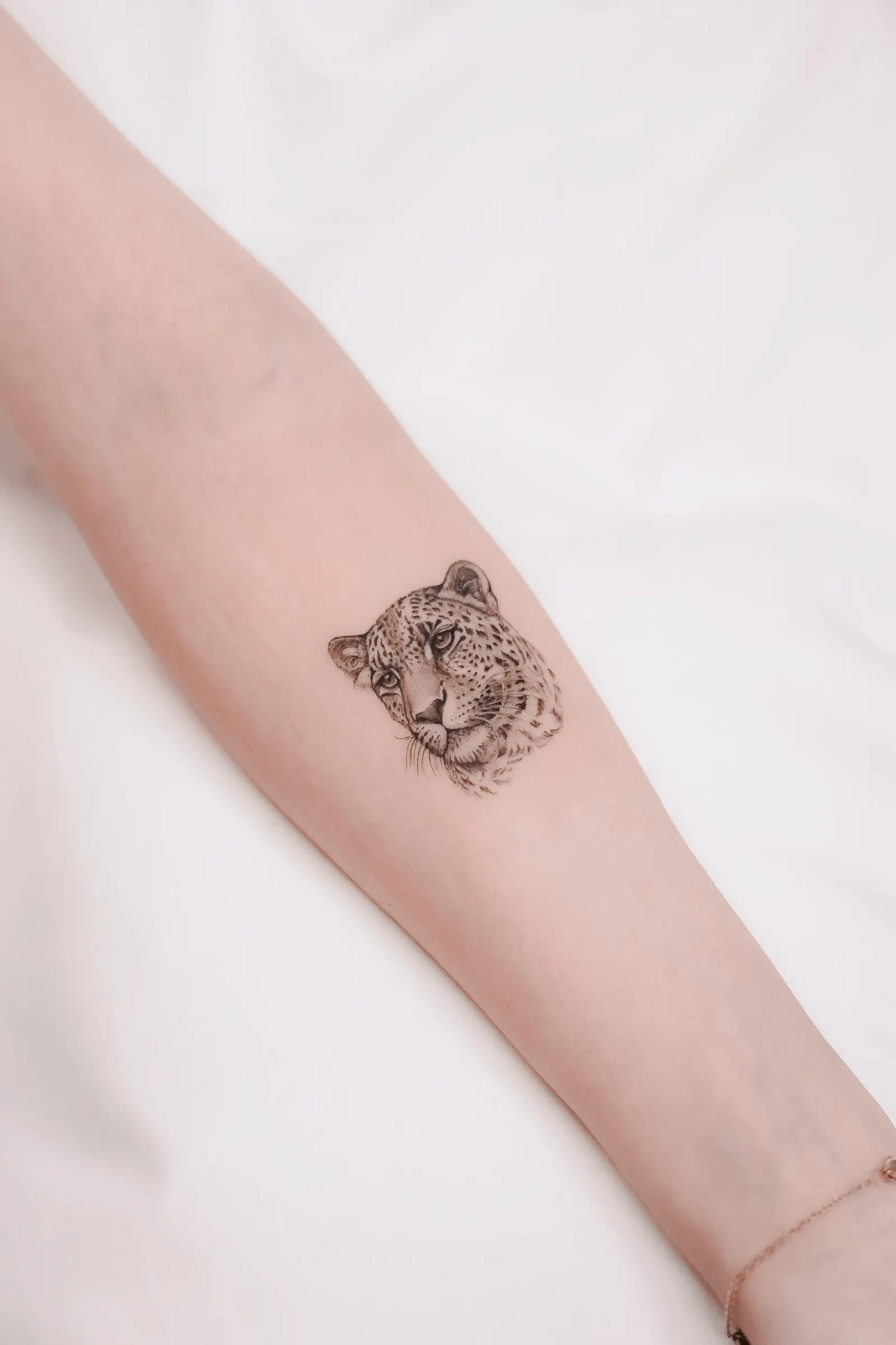 Small finely detailed leopard head tattooed on the forearm against white fabric.