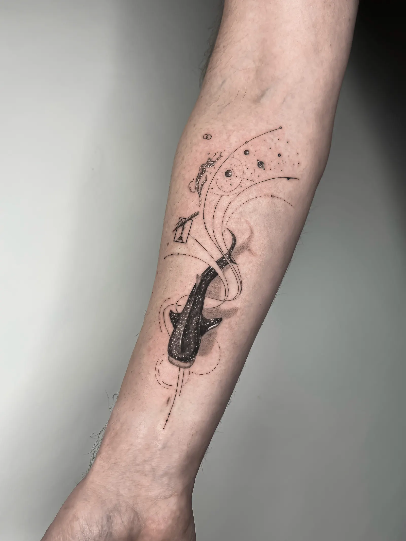 Fine-line forearm tattoo of a whale shark with planets and thin orbital lines.