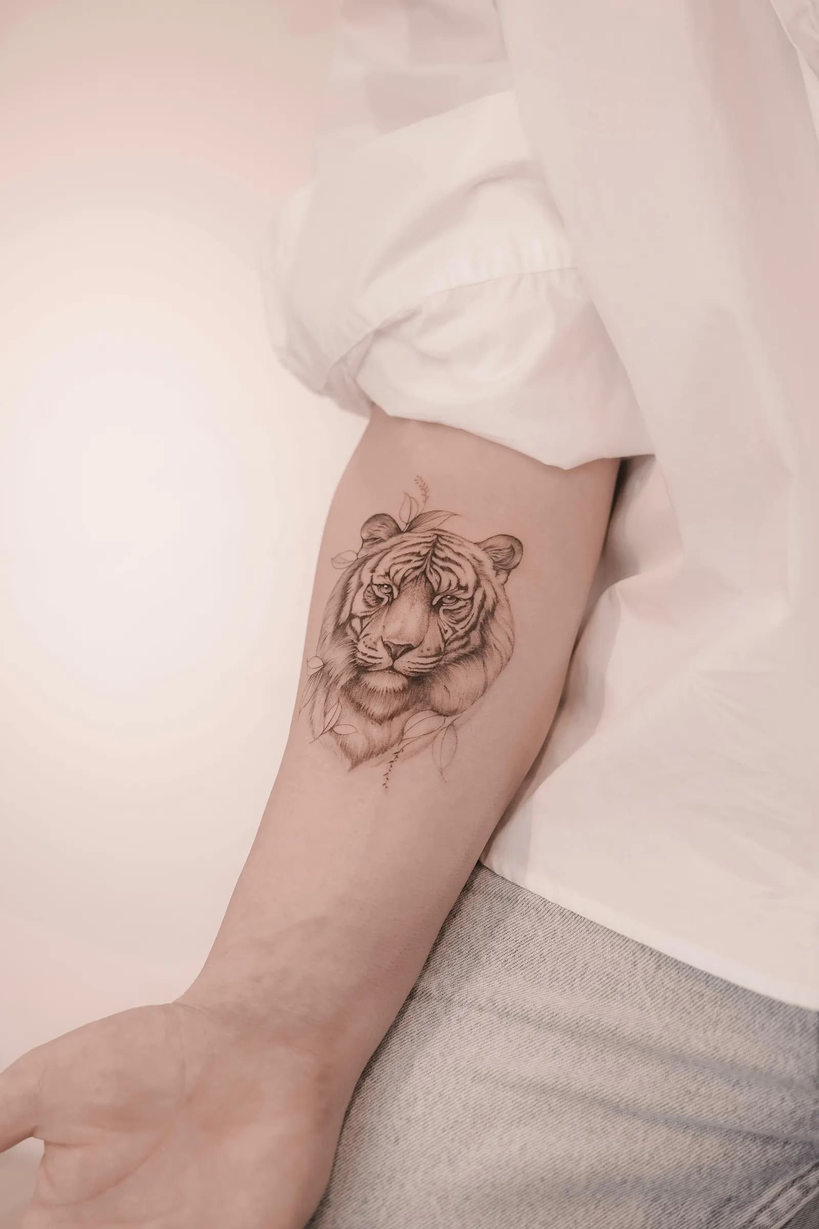 Softly shaded tiger head with small leaves, tattooed on the inner forearm.