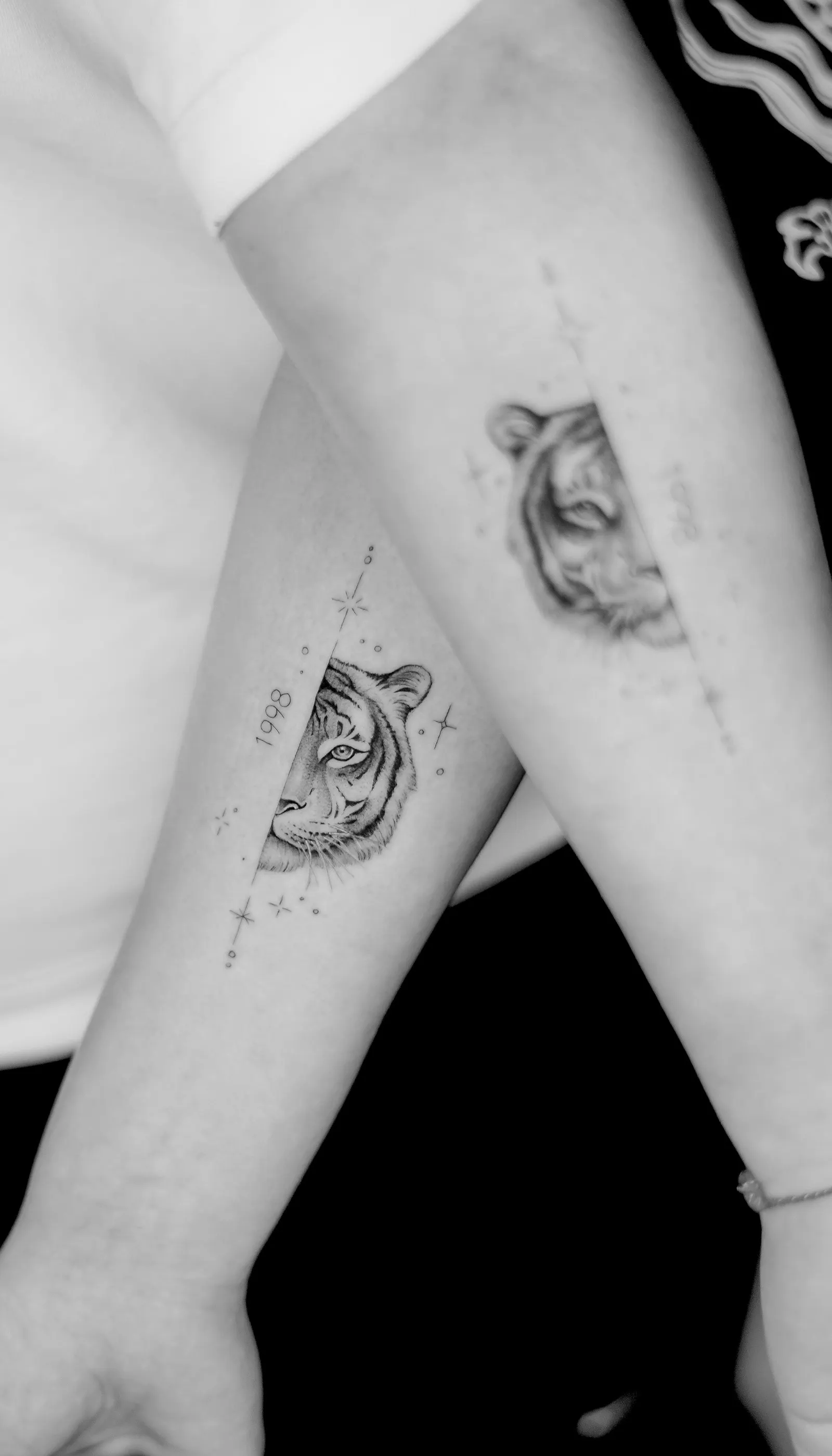 Two forearms side by side with matching tiger-head tattoos and the numerals 1998.