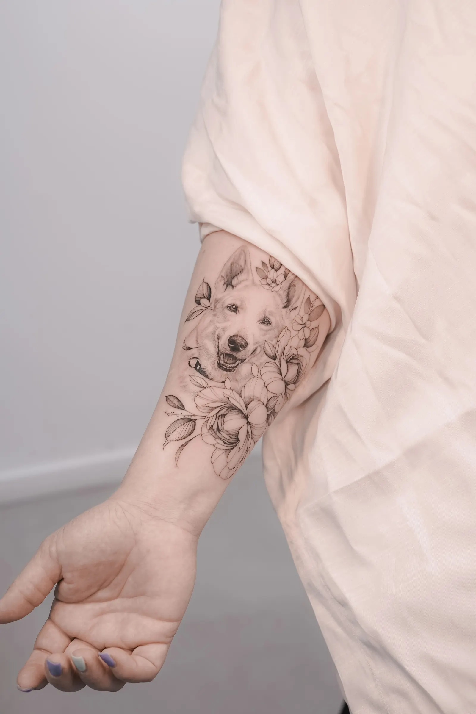 Fine-line forearm tattoo of a dog's face surrounded by flowers and leaves.