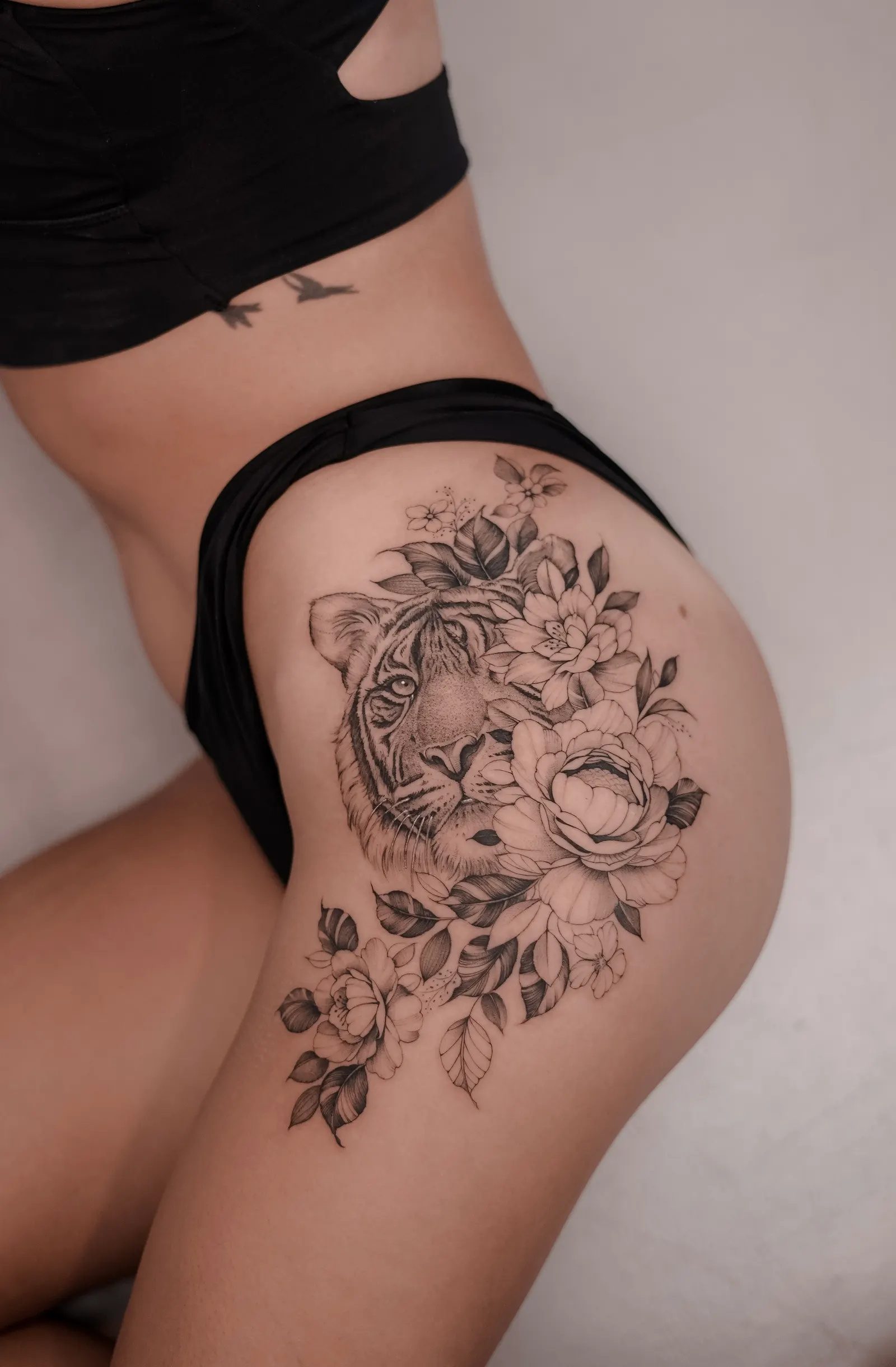 Tiger face framed by large flowers and leaves, tattooed across the hip and thigh.