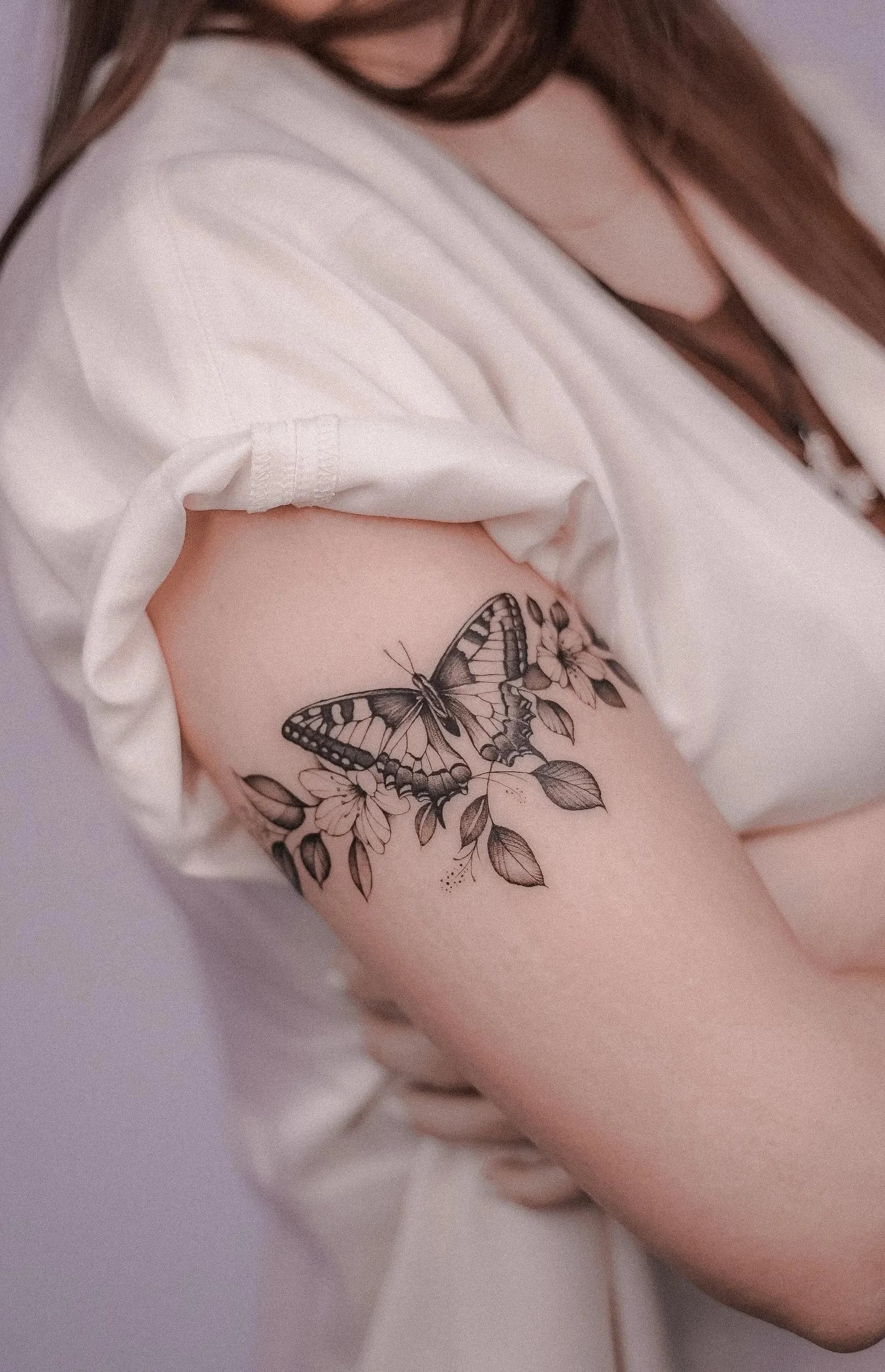 Black and grey butterfly and blossom tattoo on a woman's upper arm.