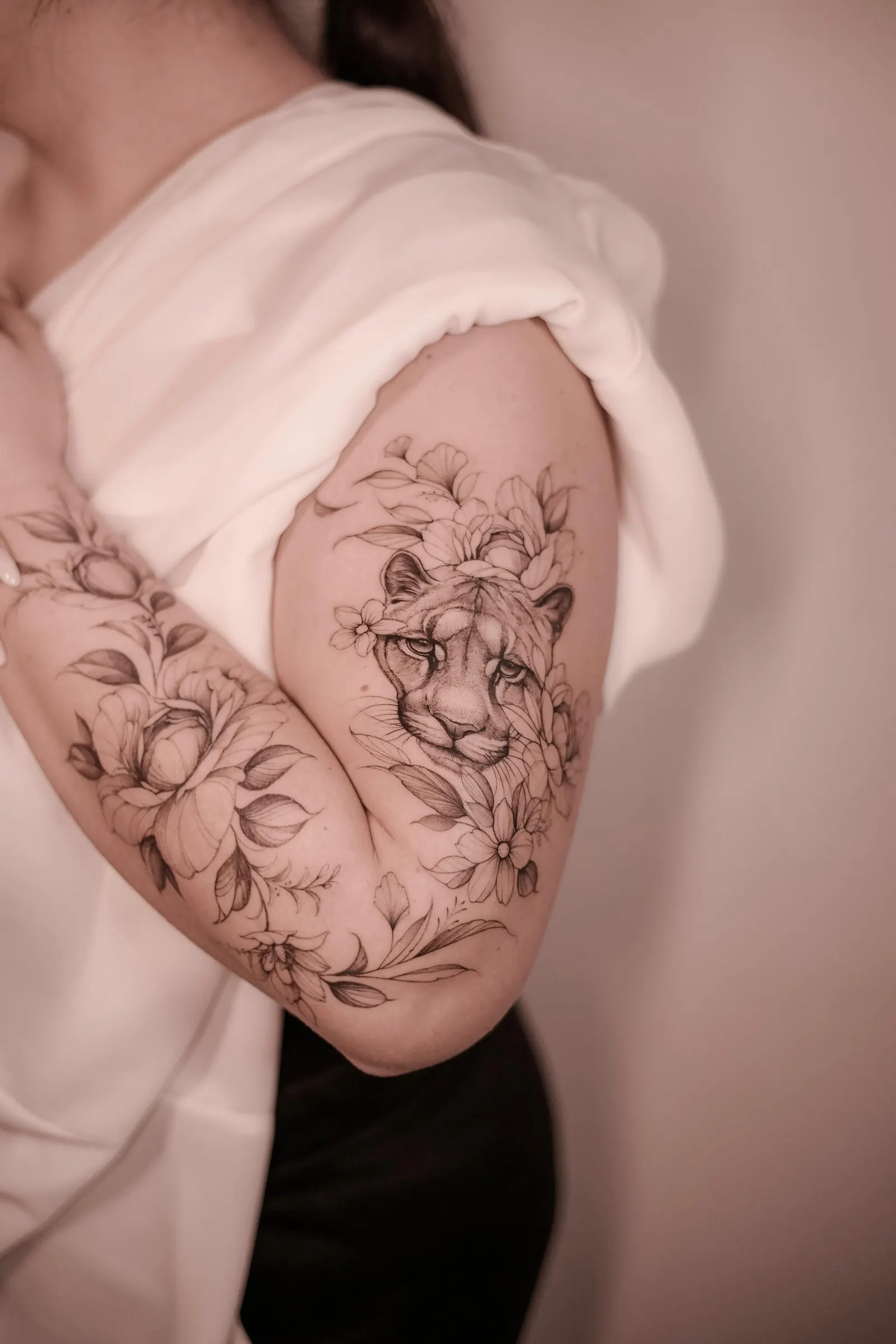 Big cat portrait surrounded by fine-line flowers on the outer upper arm and shoulder.