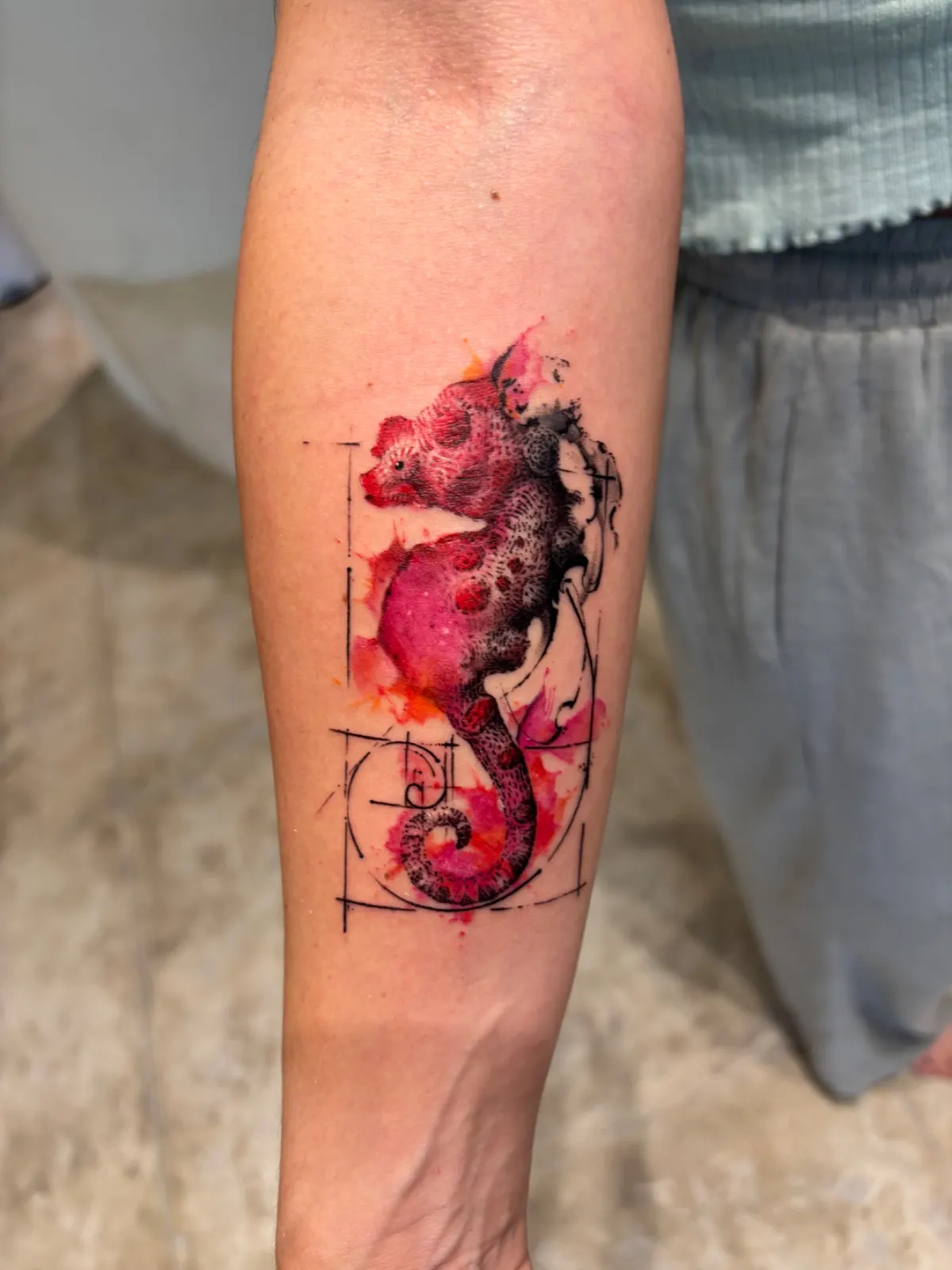 Watercolour-style animal tattoo in red and black ink with line accents on a forearm.