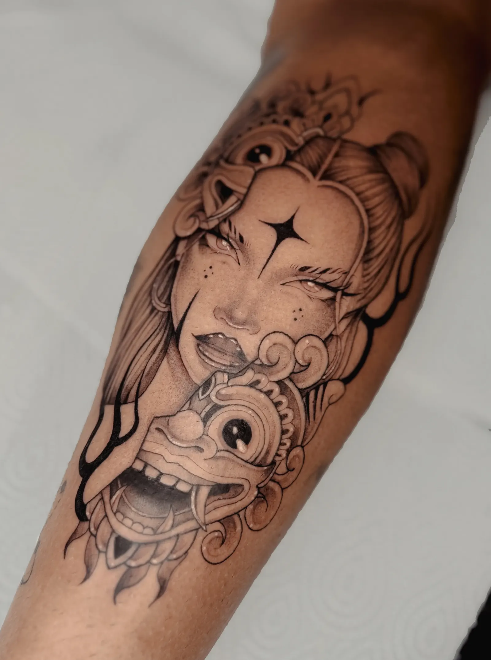 Black-and-grey tattoo of a woman with an ornate mask covering a forearm.