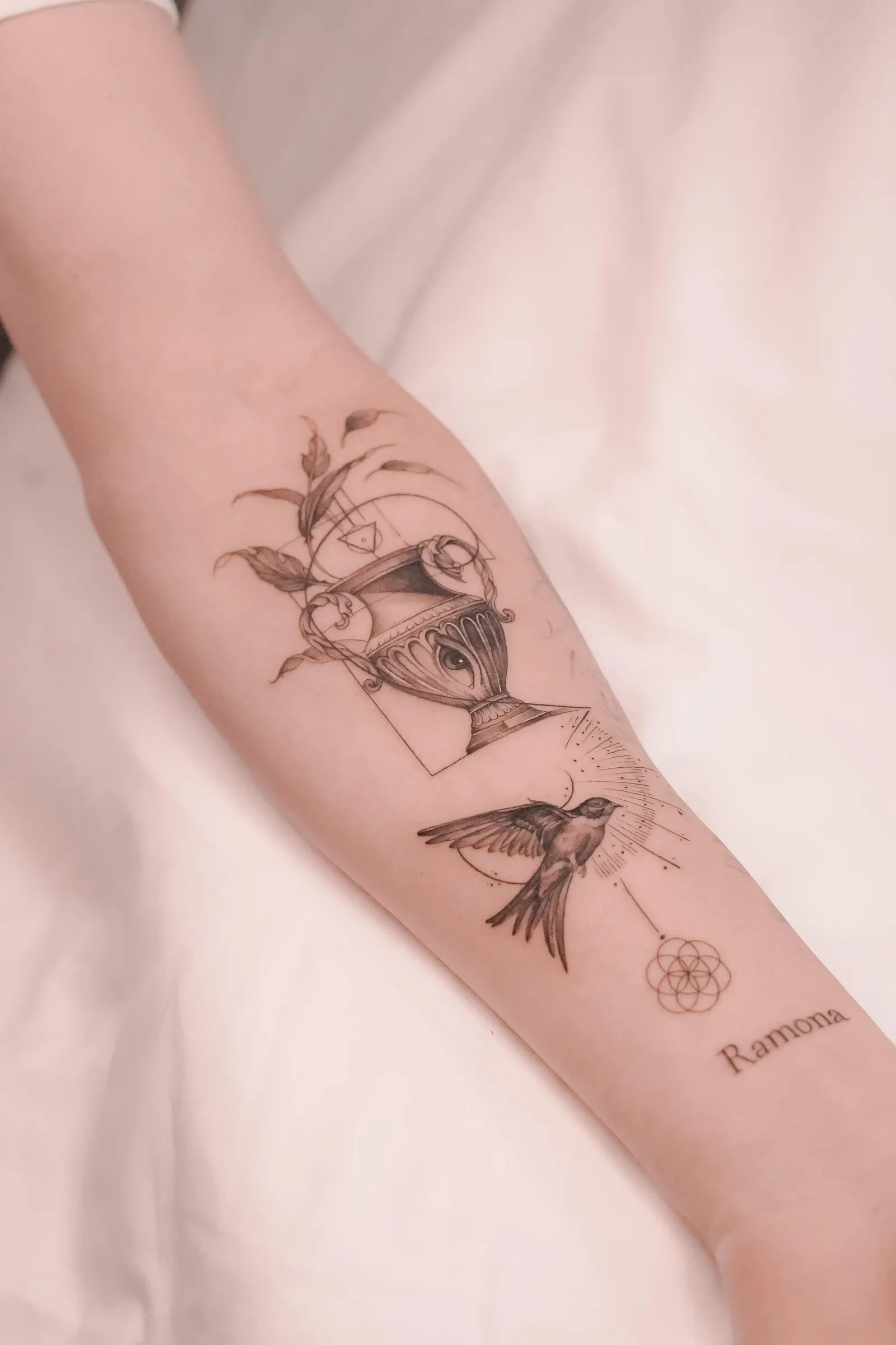 Forearm design with an ornate goblet, a swallow, geometric line shapes and a small name.