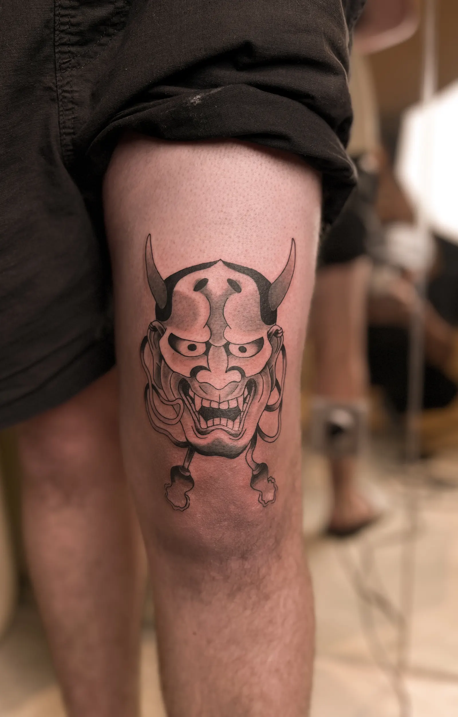Black-and-grey horned mask tattoo on a thigh above the knee.