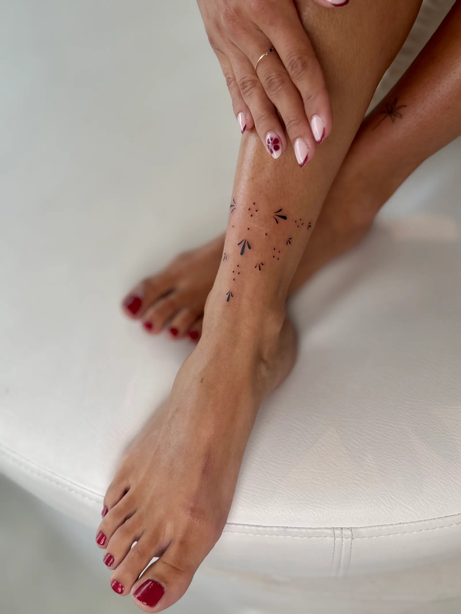 Scattered fine-line dot and petal ornaments tattooed along an ankle and lower leg.