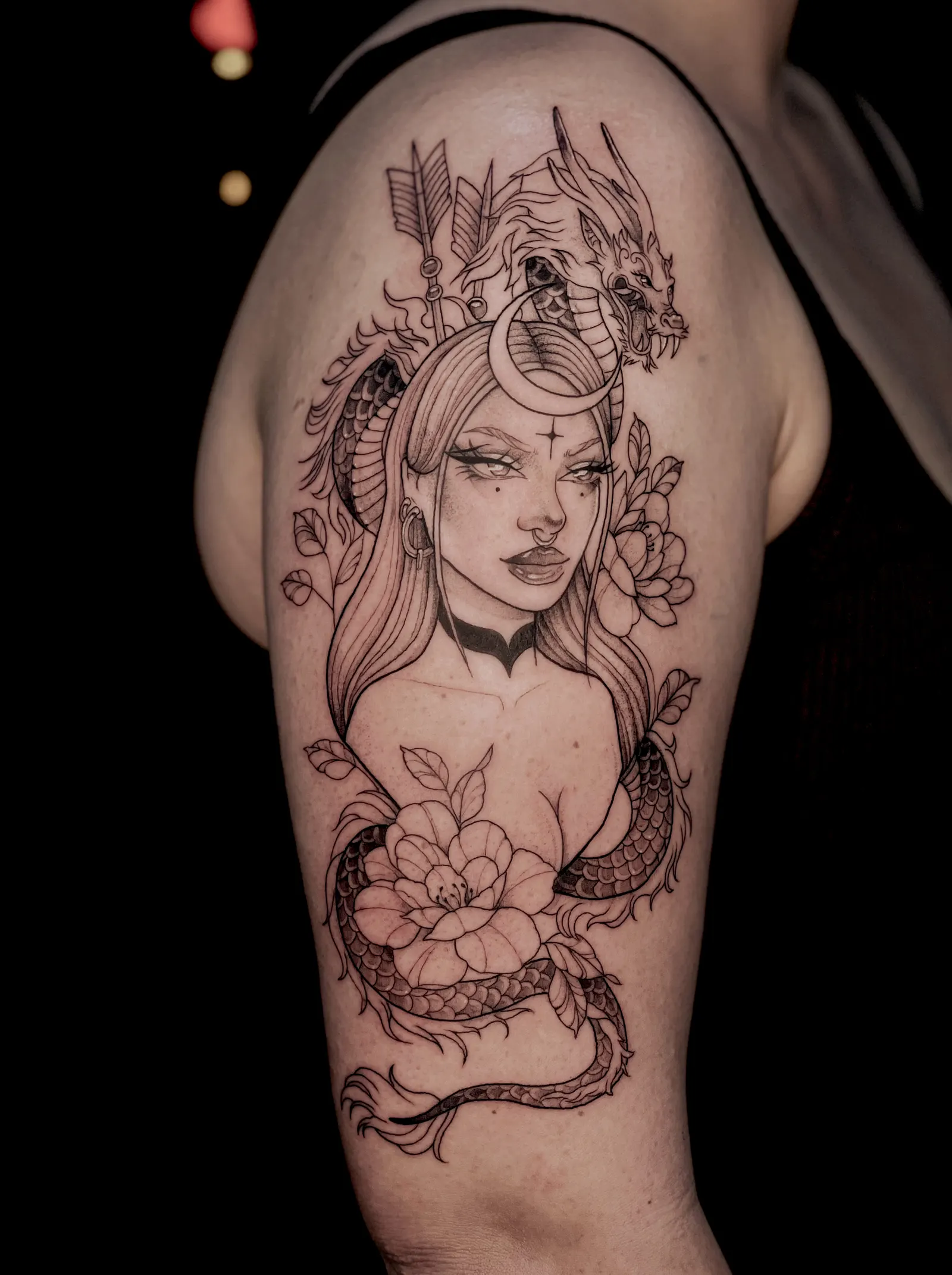 Large fine-line tattoo of a woman with a dragon and peonies covering an upper arm.
