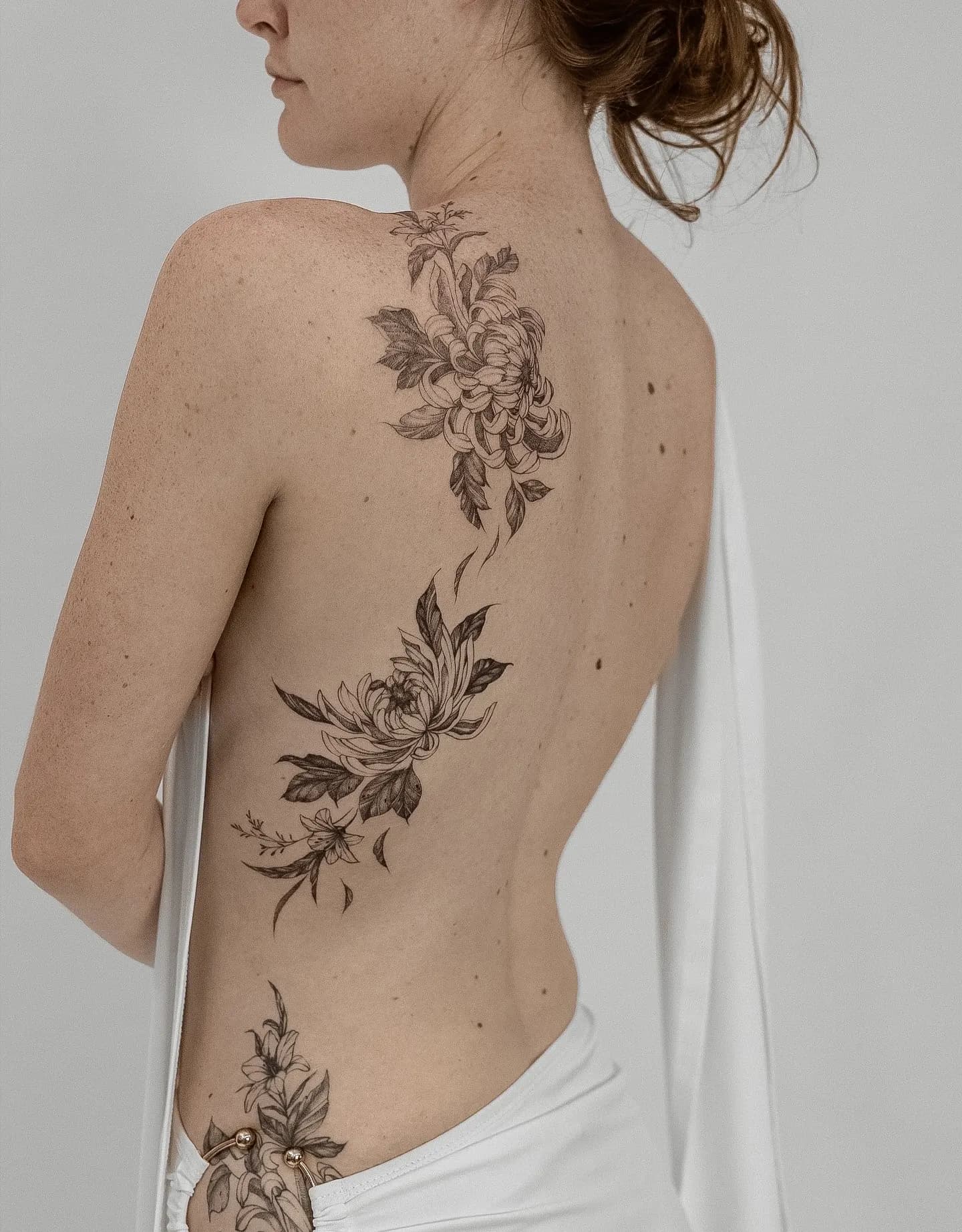 Large fine-line chrysanthemum and leaf tattoo flowing down the back and side of the torso.