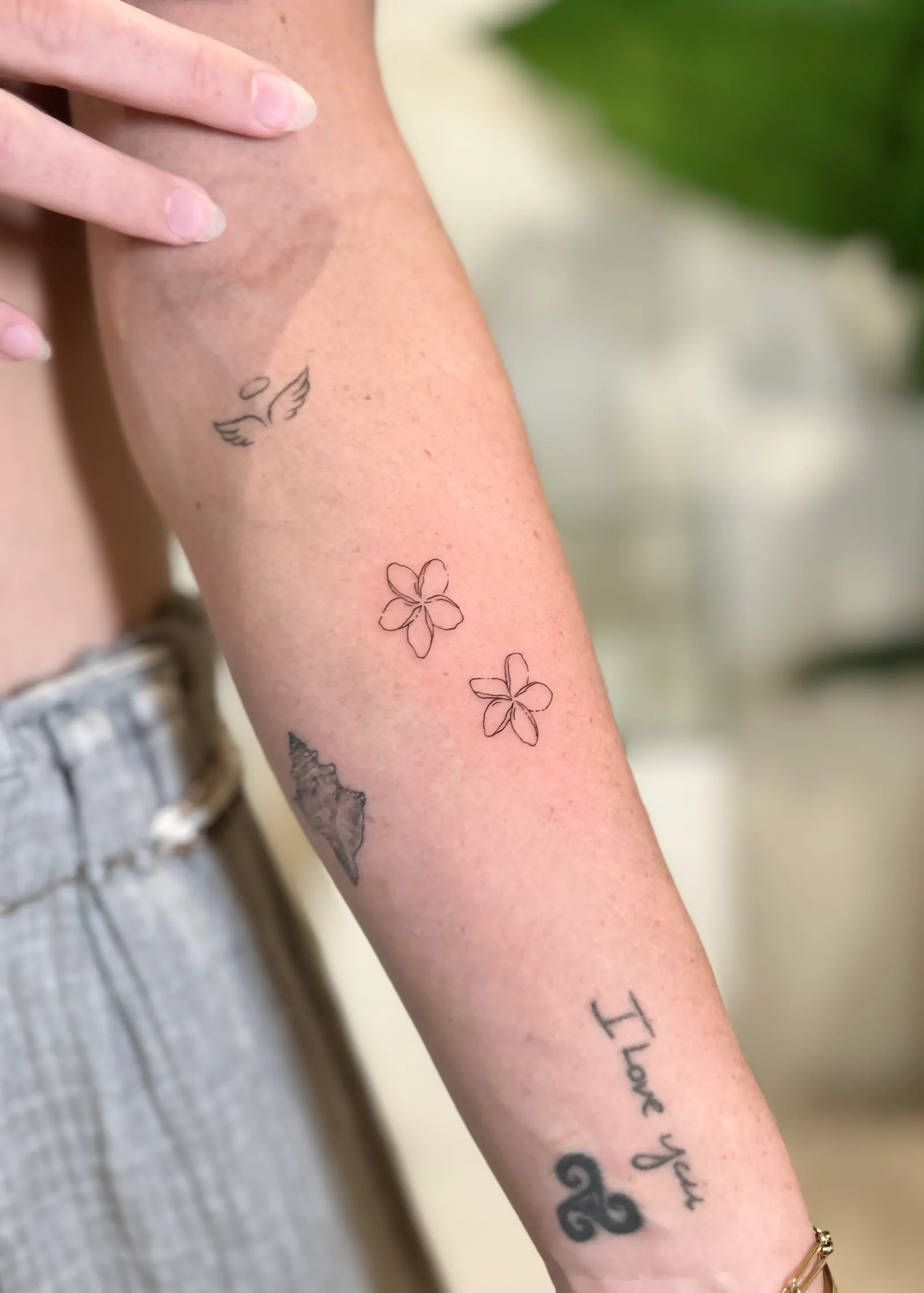 Two outlined frangipani flowers tattooed on a forearm among other small tattoos.