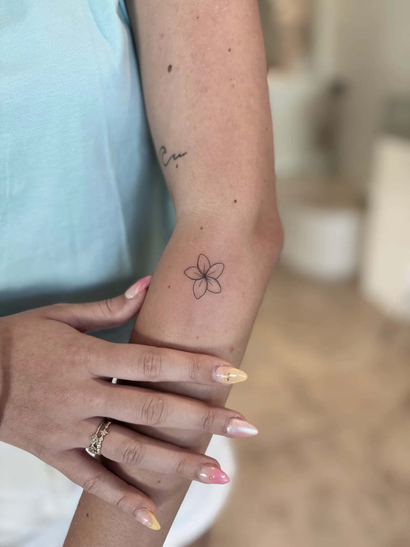 Small outlined frangipani flower tattooed on an arm.