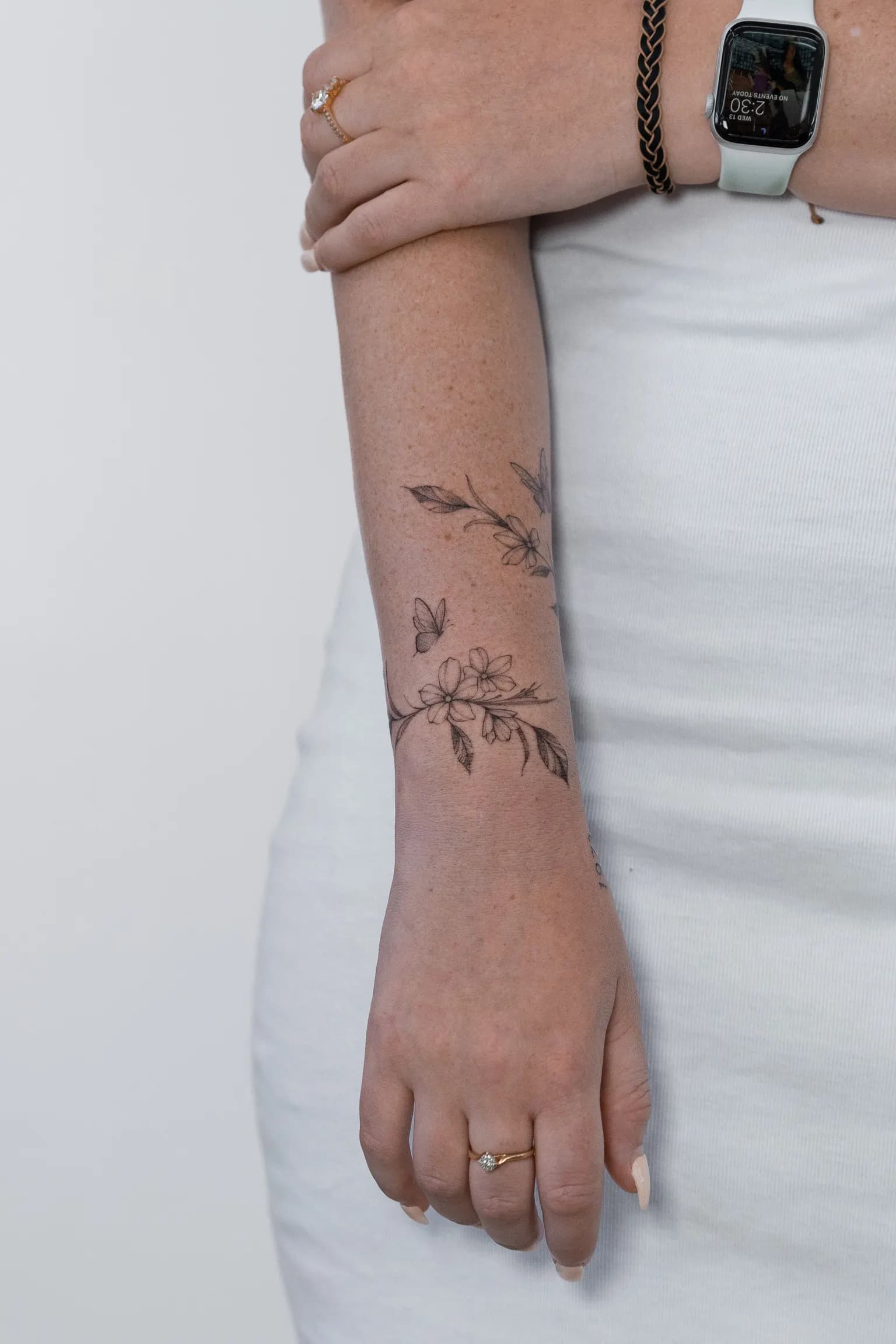 Fine-line floral branch tattoo wrapping around a forearm down toward the wrist.