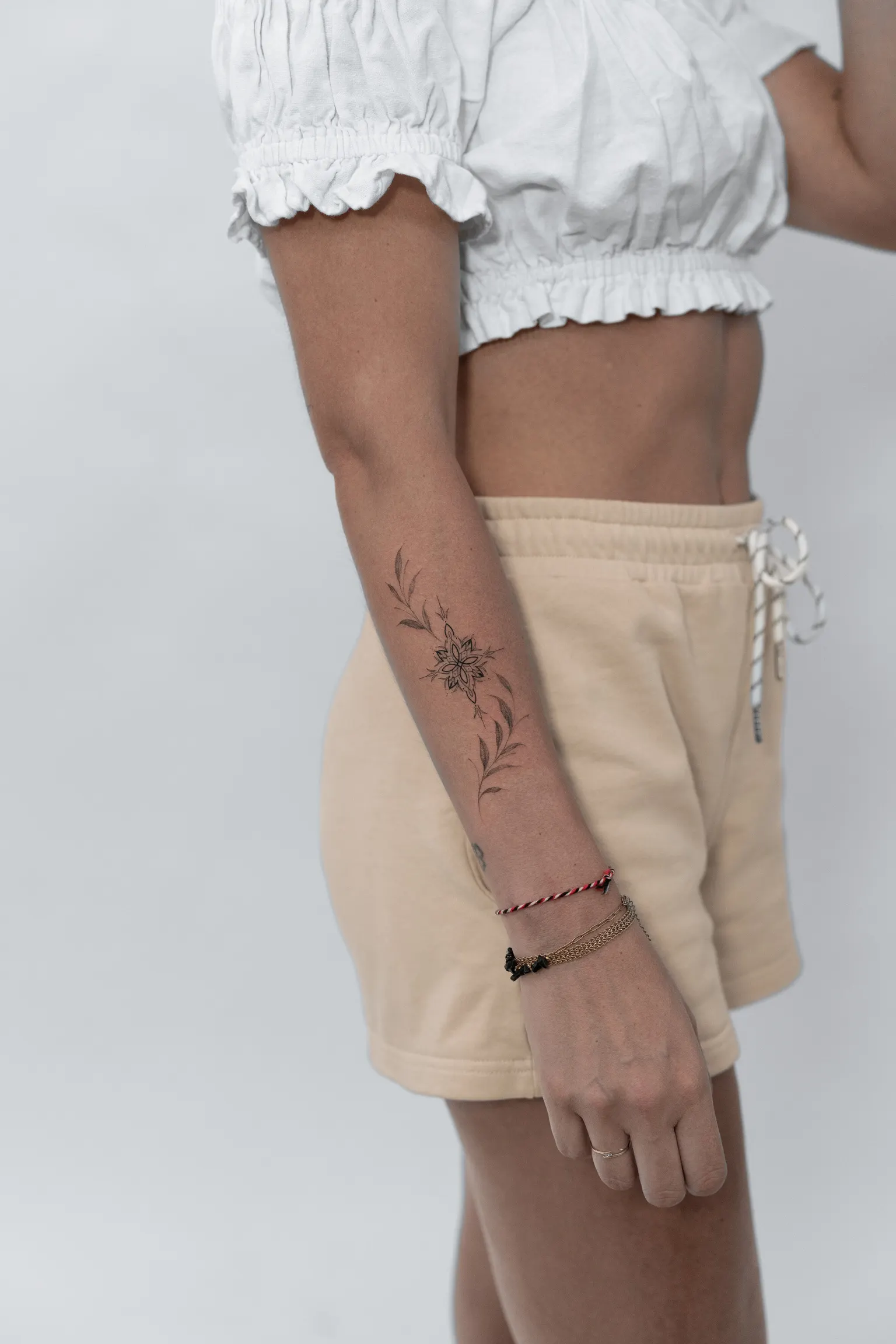 Fine-line floral and mandala tattoo wrapping around a forearm near the wrist.