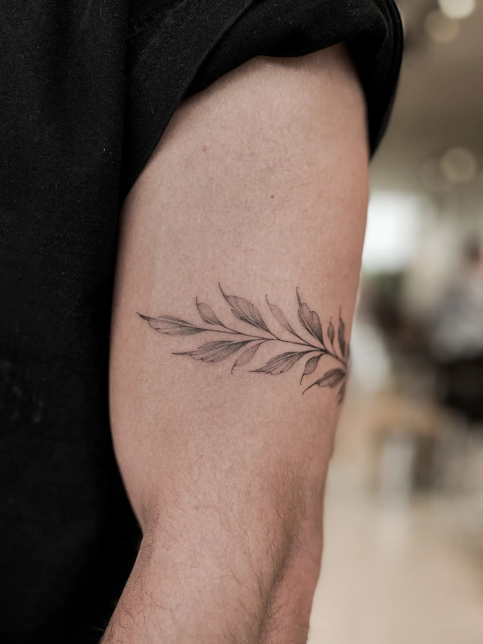 Fine-line leafy branch tattoo wrapping around a person's upper arm.