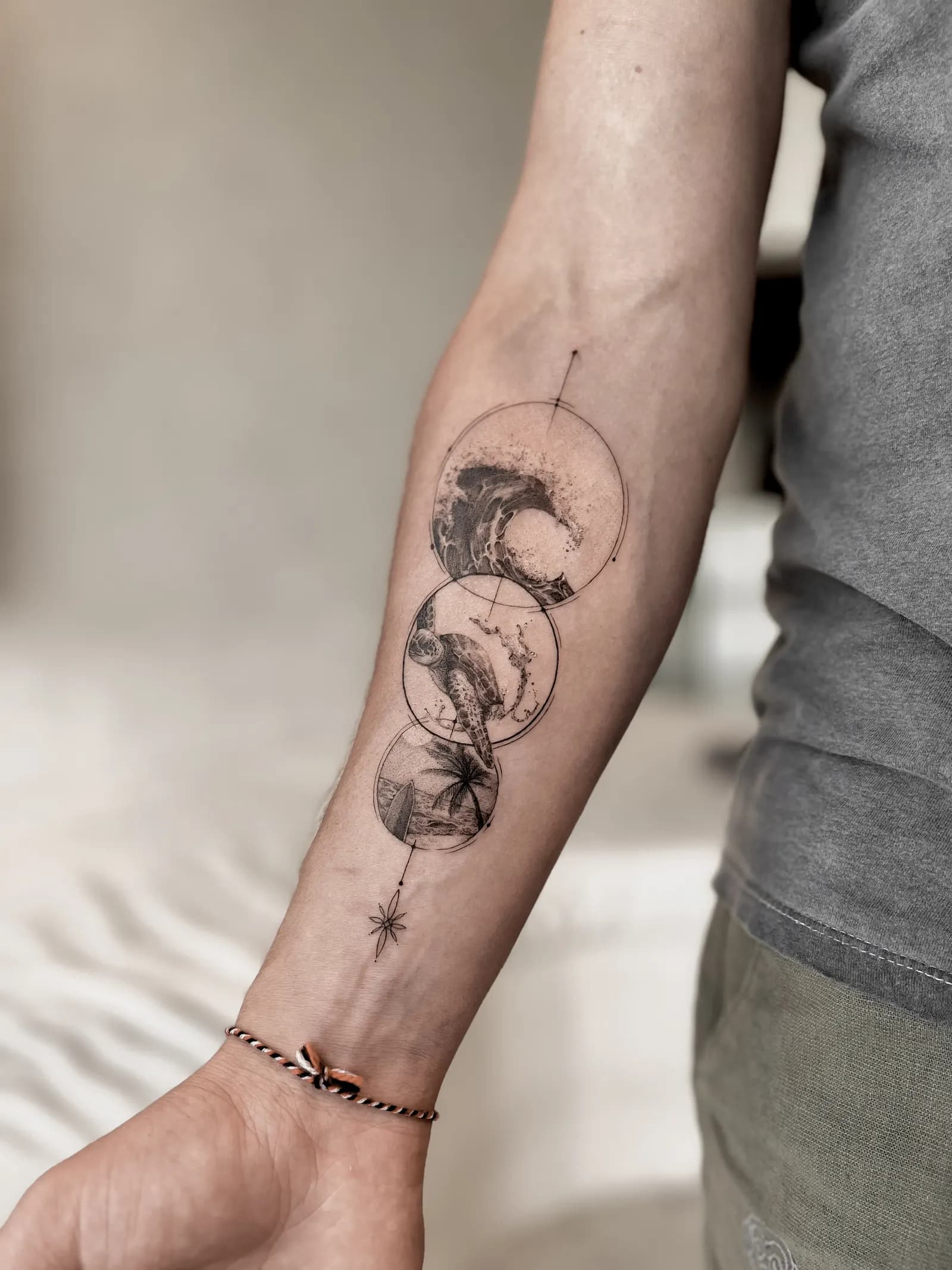 Three linked circles holding a wave, a sea turtle and palm trees on a forearm.