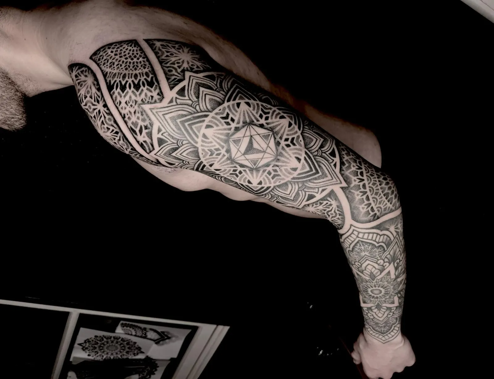 Geometric mandala sleeve tattoo covering an arm, shot against a dark background.