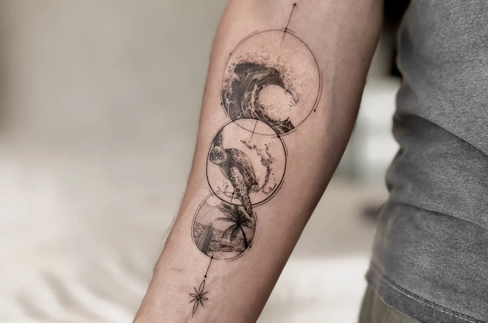 Three overlapping circles tattooed on a forearm showing a wave, a sea turtle and a beach scene.