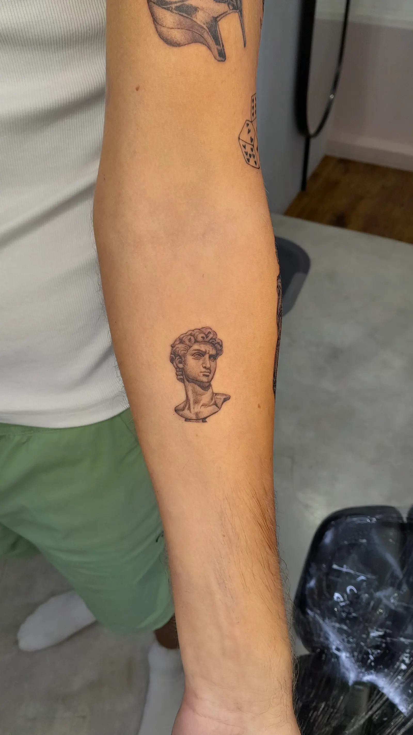 Small black and grey tattoo of a classical marble bust on a forearm.