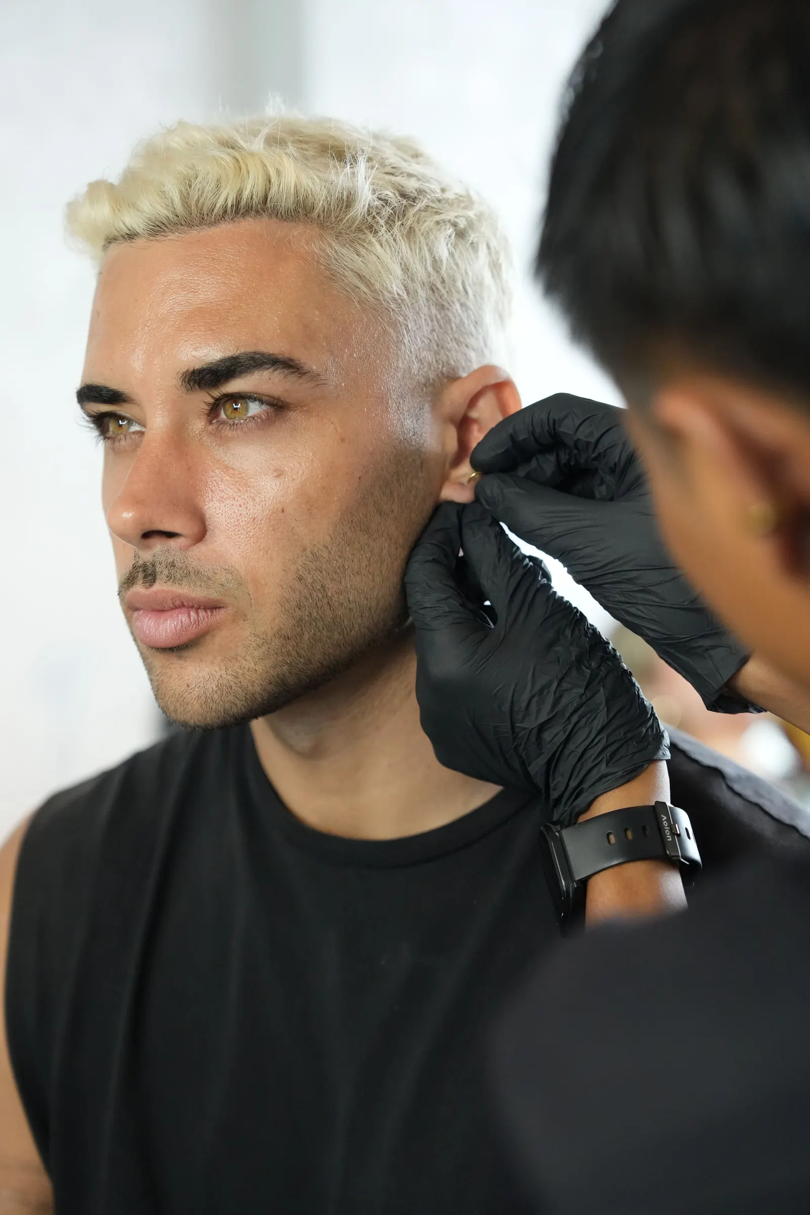 Gloved hands working at a man's ear lobe during an ear piercing.