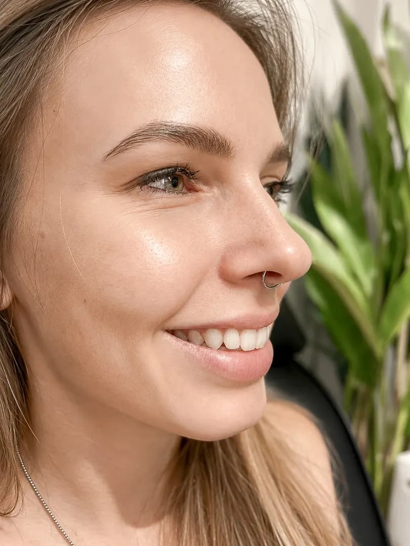 Close-up of a smiling person wearing a small silver nose hoop.