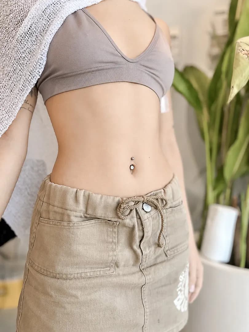 Close-up of a navel piercing with a jewelled barbell on a torso.