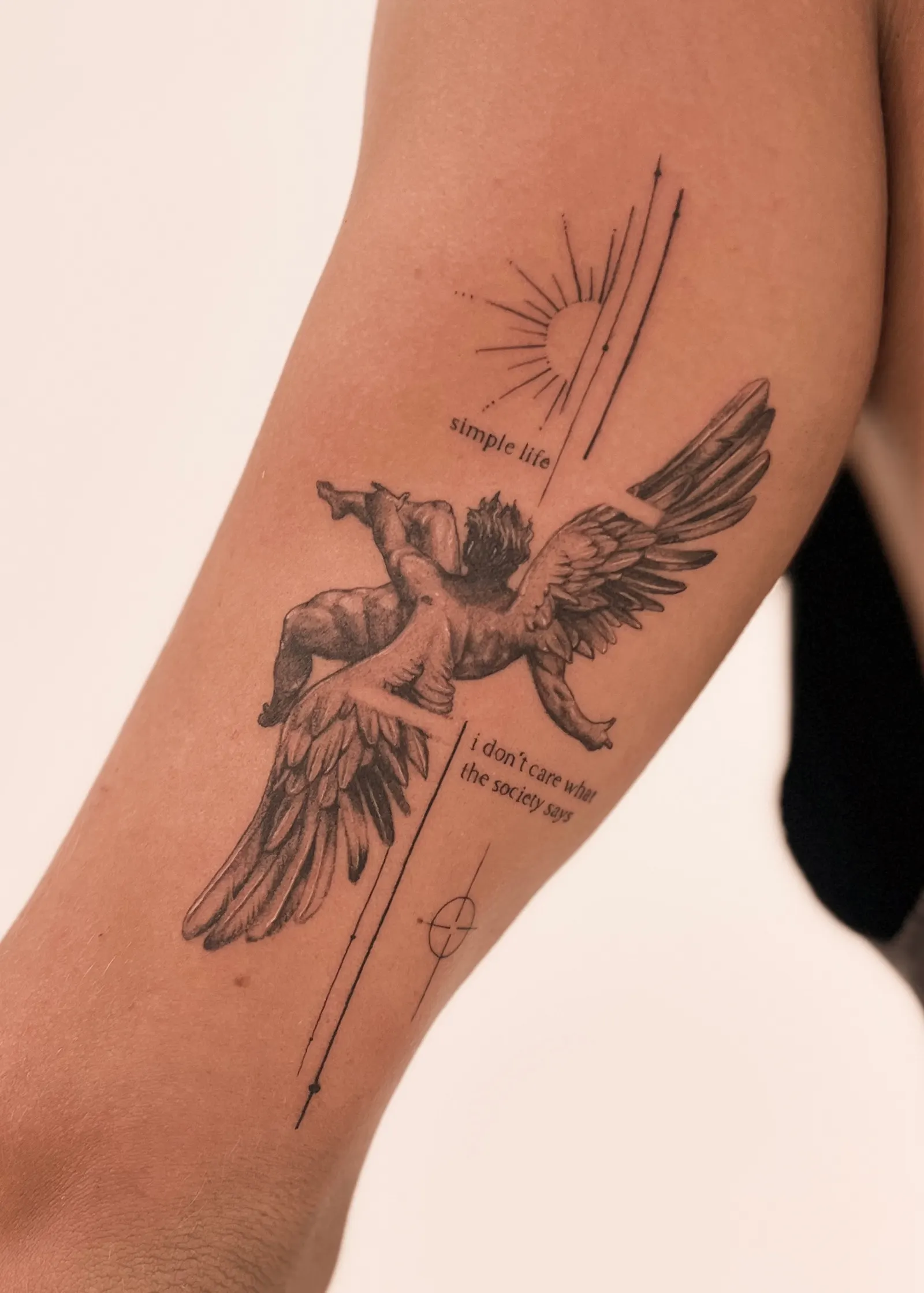 Black and grey tattoo of a winged angel figure with thin lines and two small script phrases.