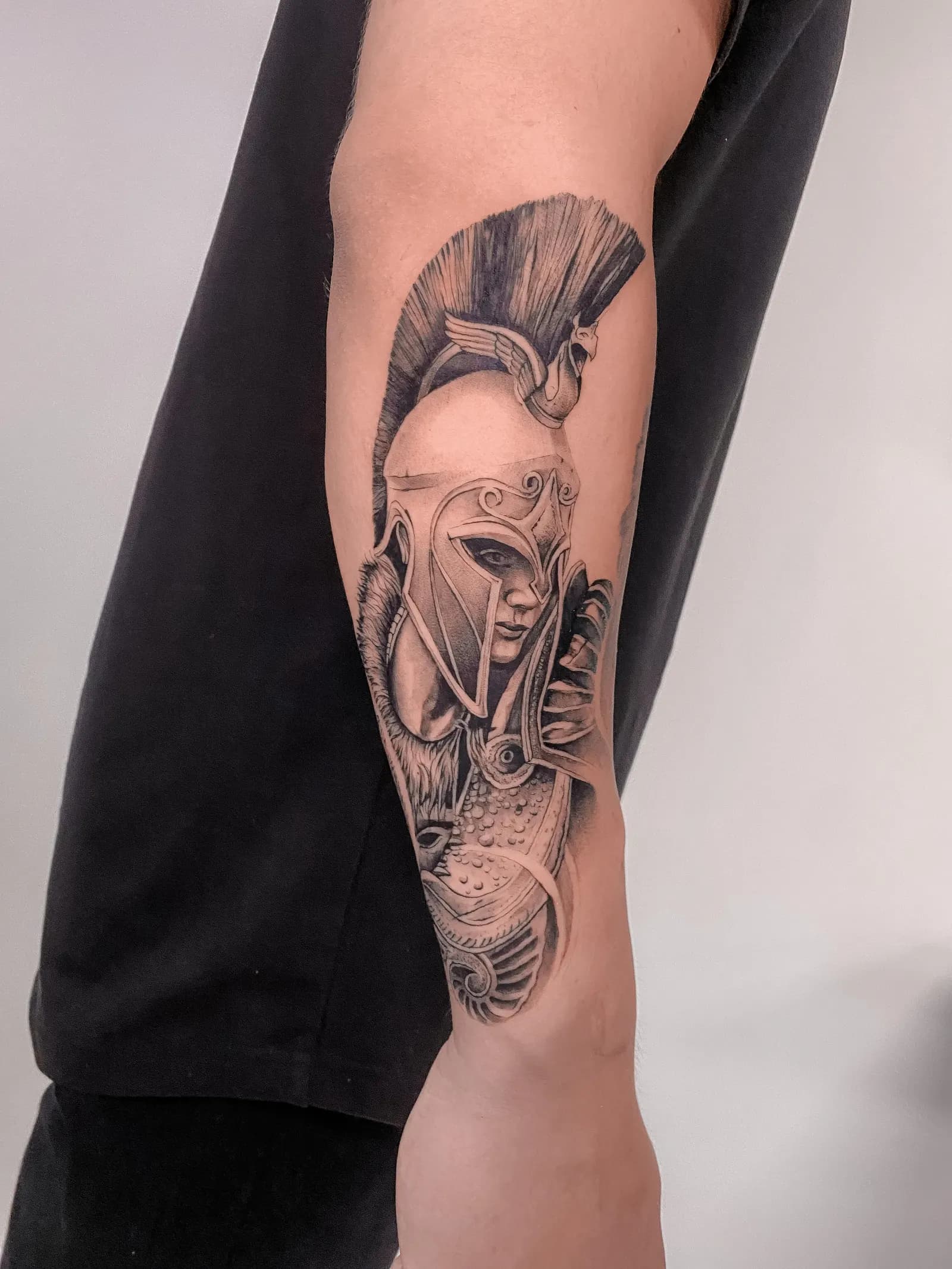 Black and grey tattoo of a helmeted warrior figure on a forearm.