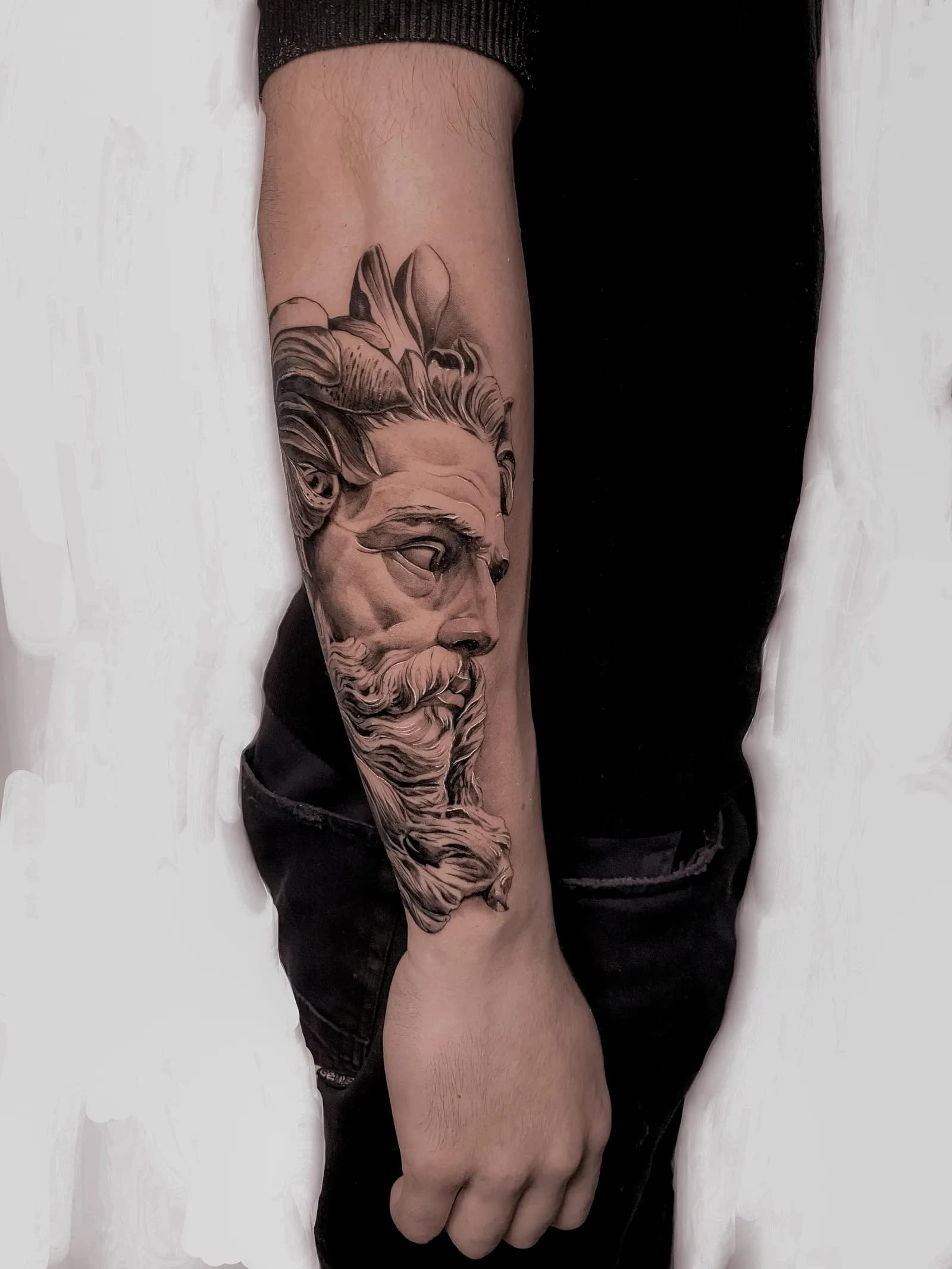 Realistic black-and-grey classical statue head tattooed on a forearm.