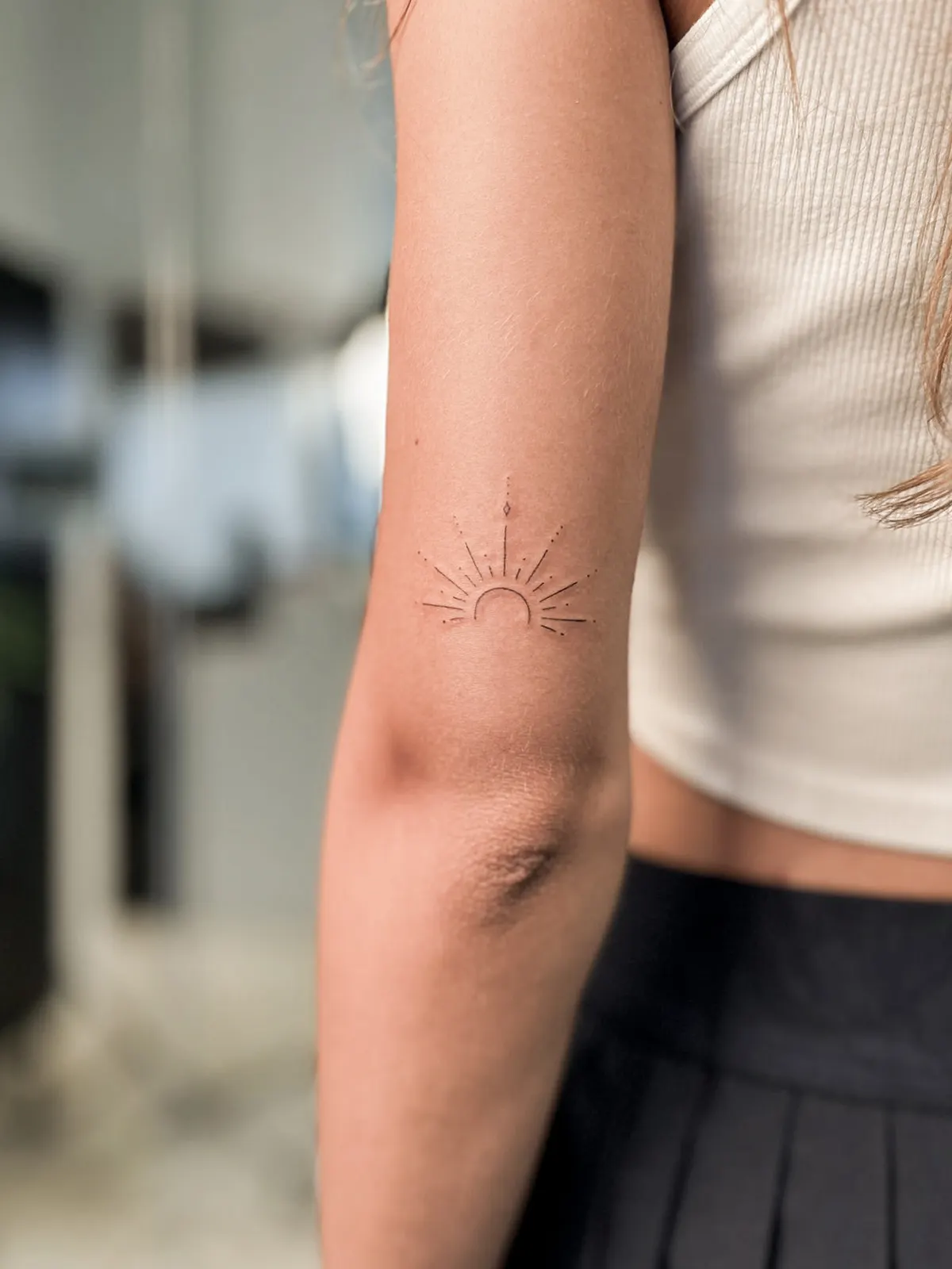 Small fine-line sunrise tattoo on the back of an upper arm.