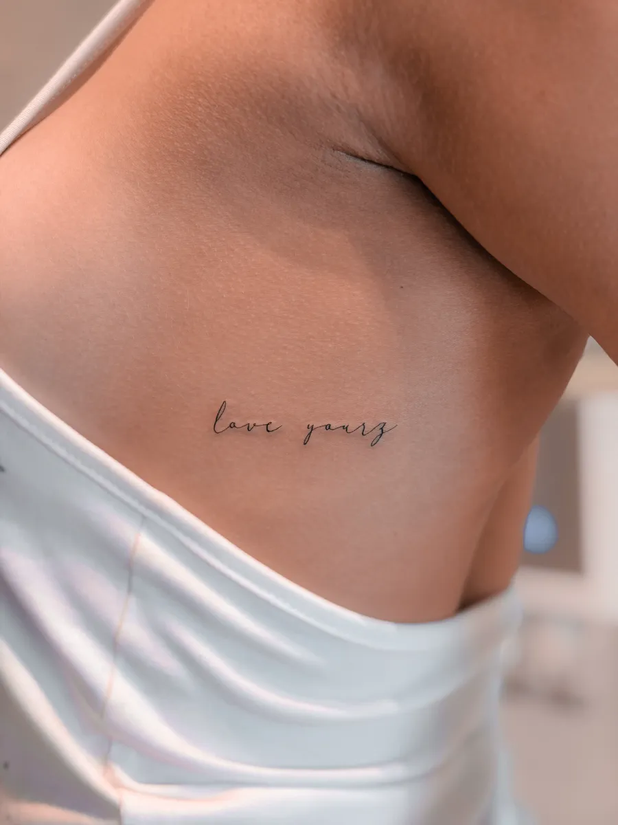 Fine line script lettering rib tattoo