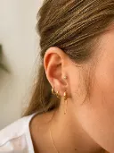 Stacked lobe piercings with gold hoops and a chain drop