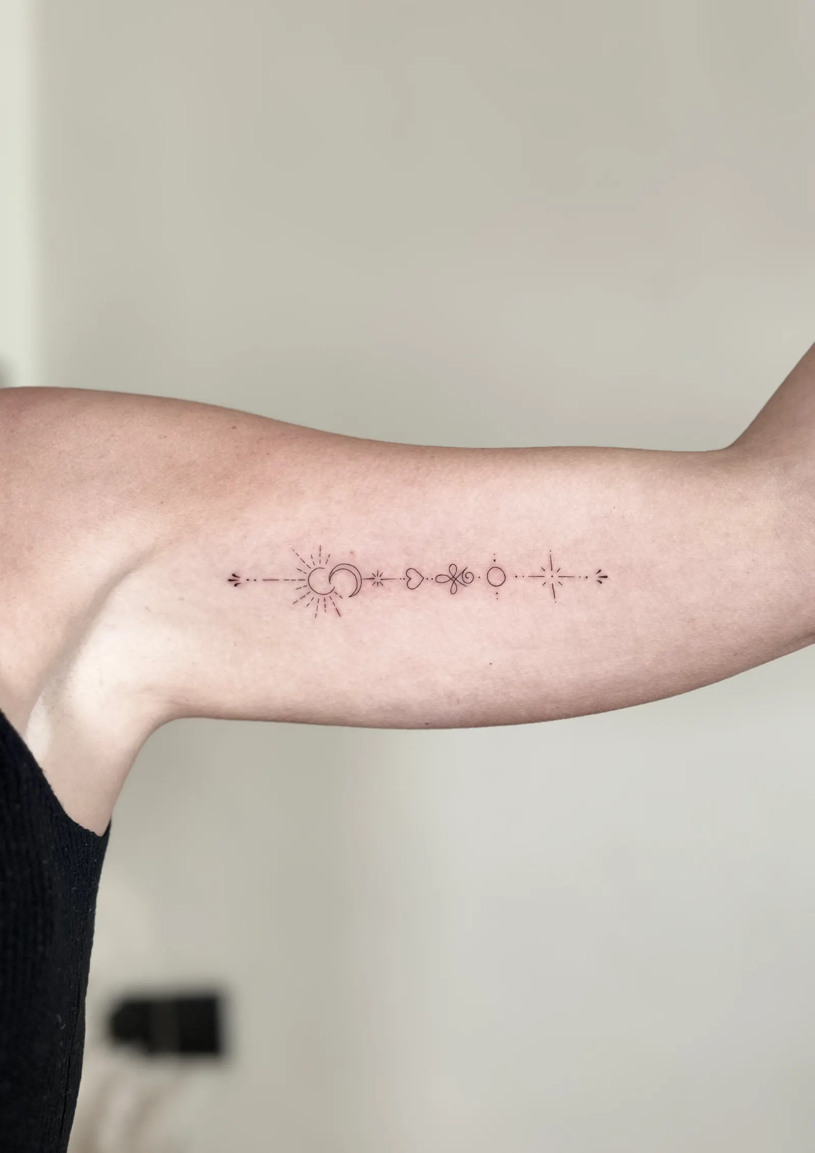 Row of fine-line symbols including a sun, moon and star tattooed on an inner upper arm.
