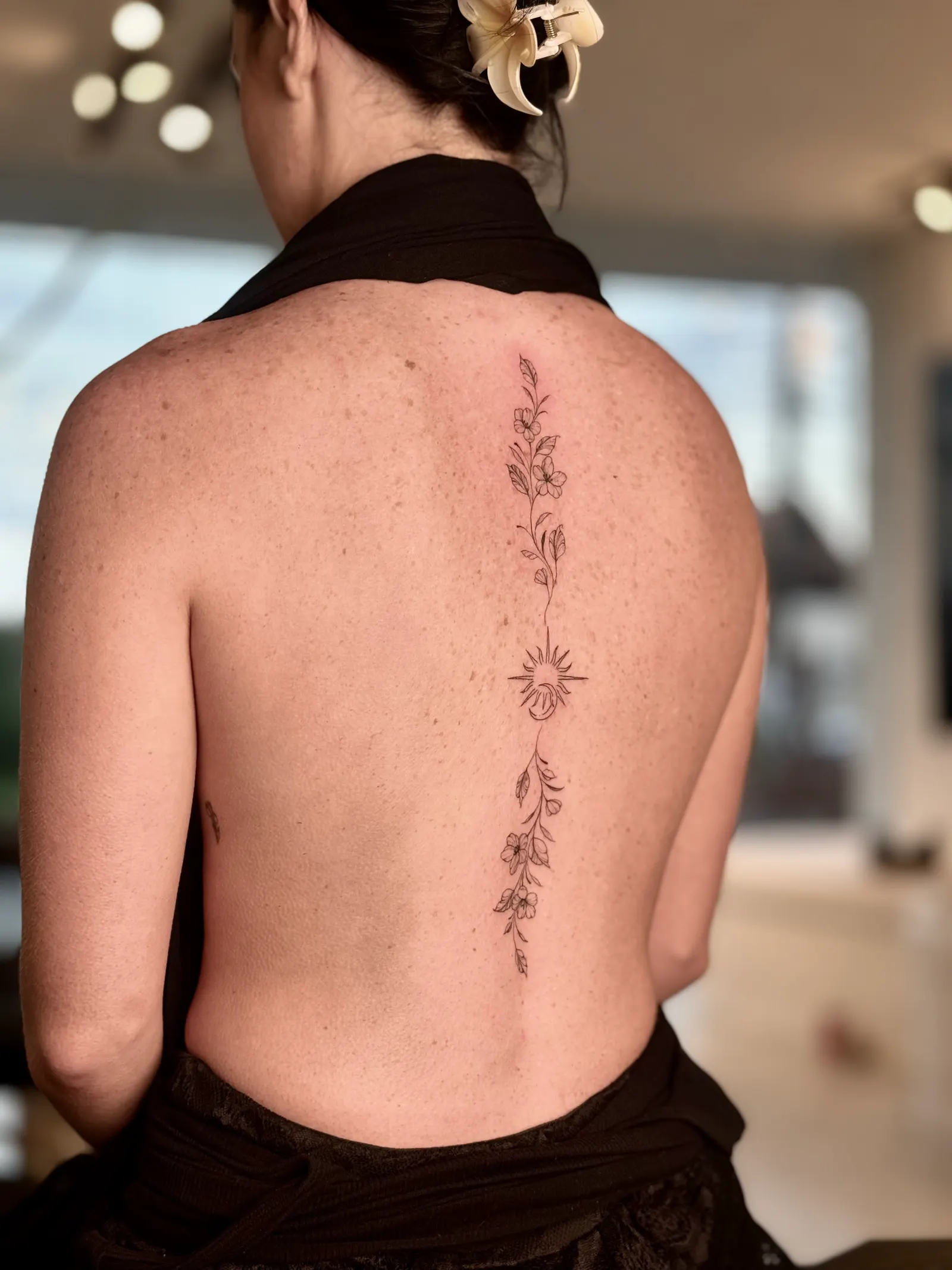 Fine-line floral stem with a sun motif running down the centre of a back.