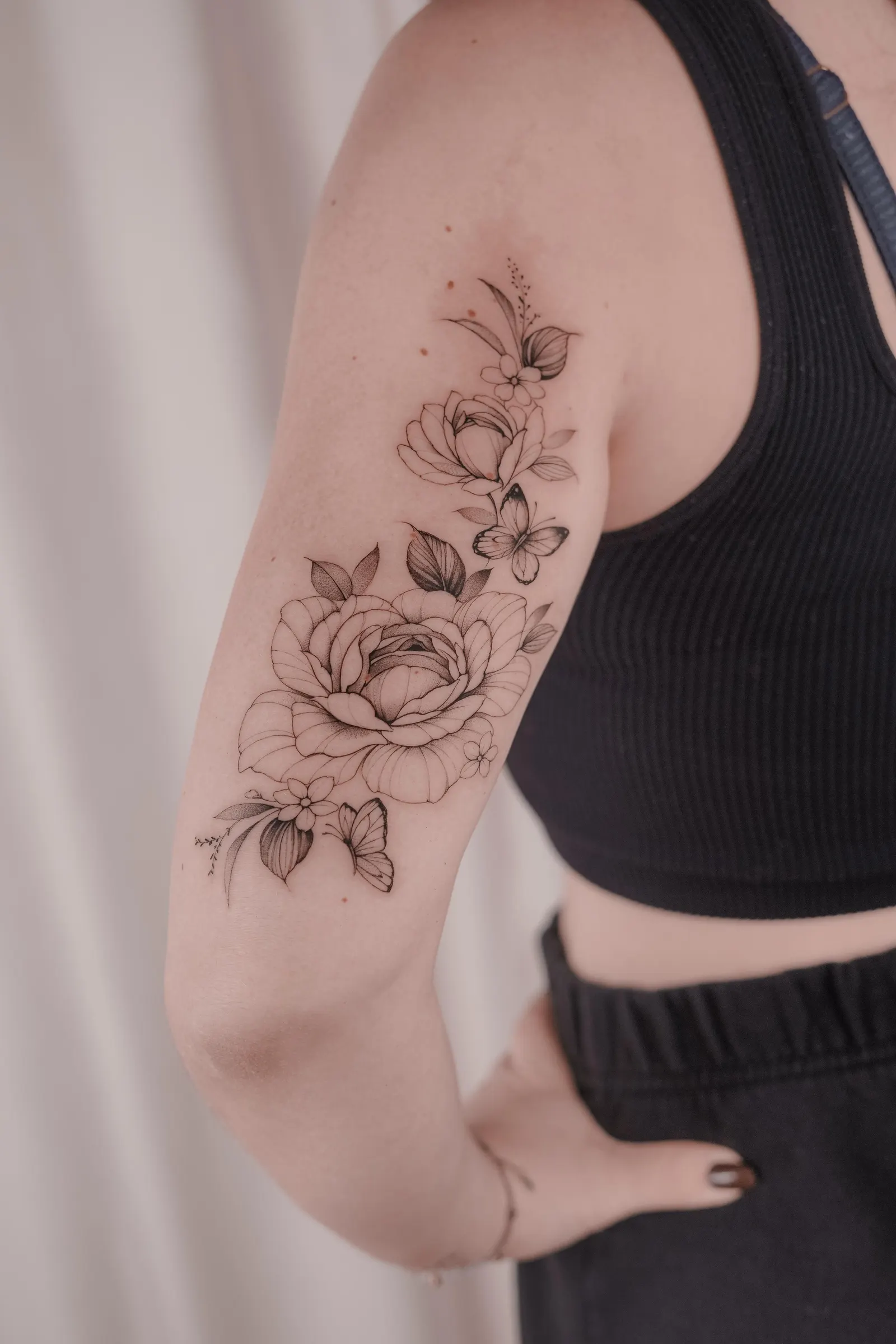 Roses, leaves and butterflies in fine black linework wrapping the upper arm.