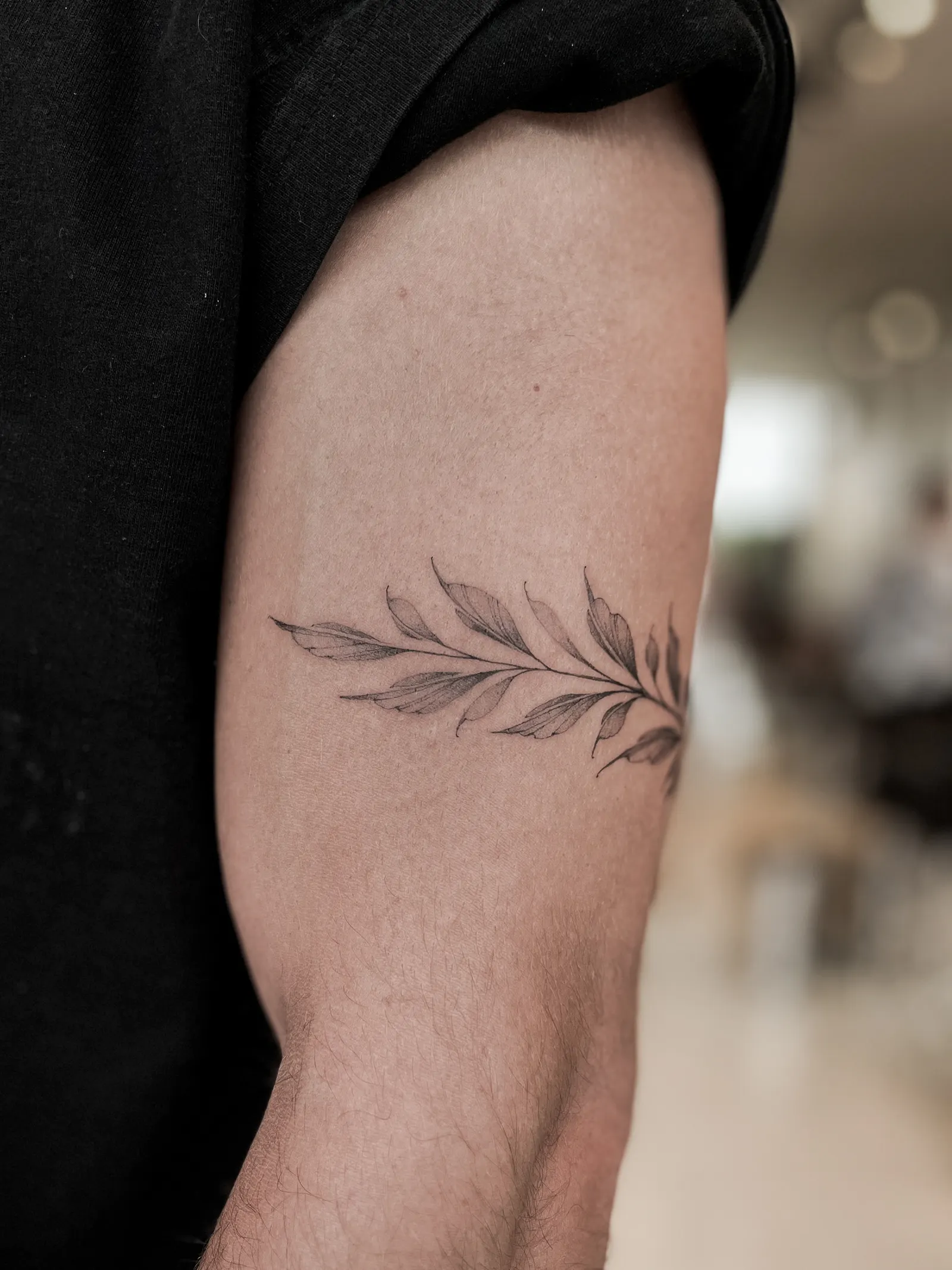 Fine-line leafy branch tattoo wrapping around a person's upper arm.