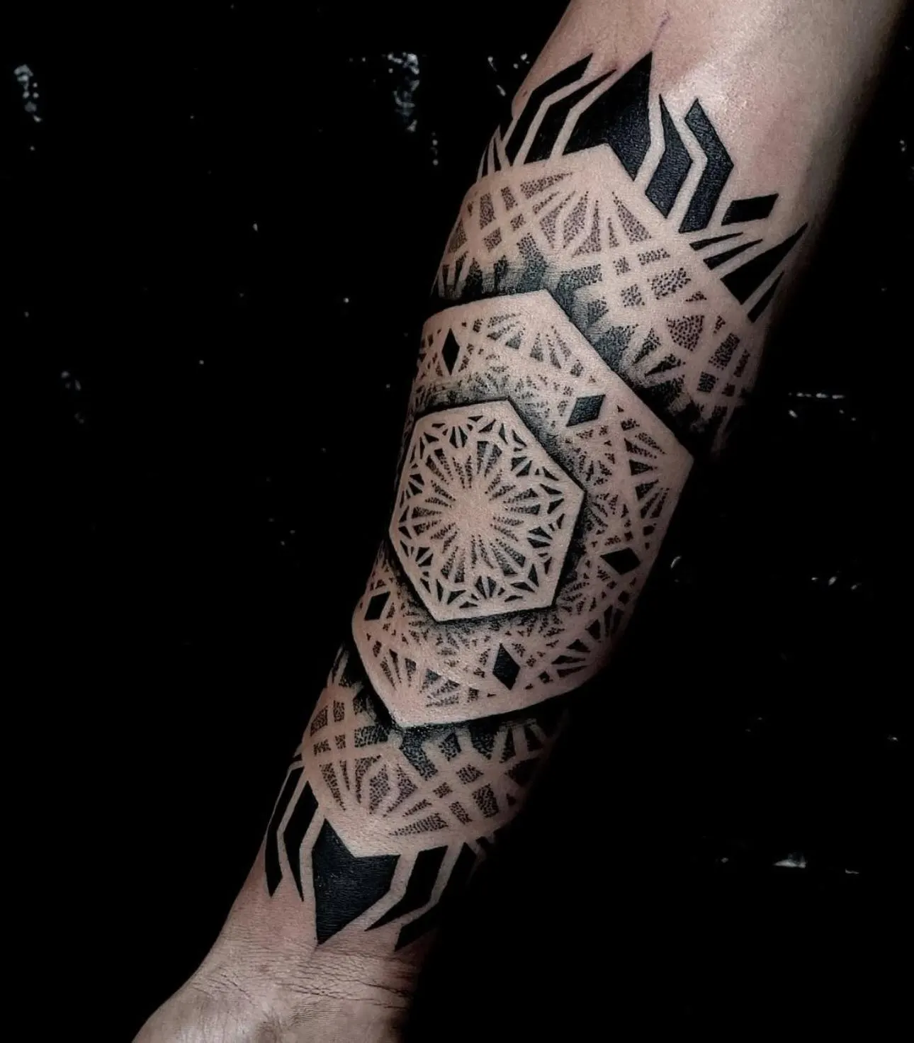 Dotwork geometric tattoo covering a forearm, shot against a black background.