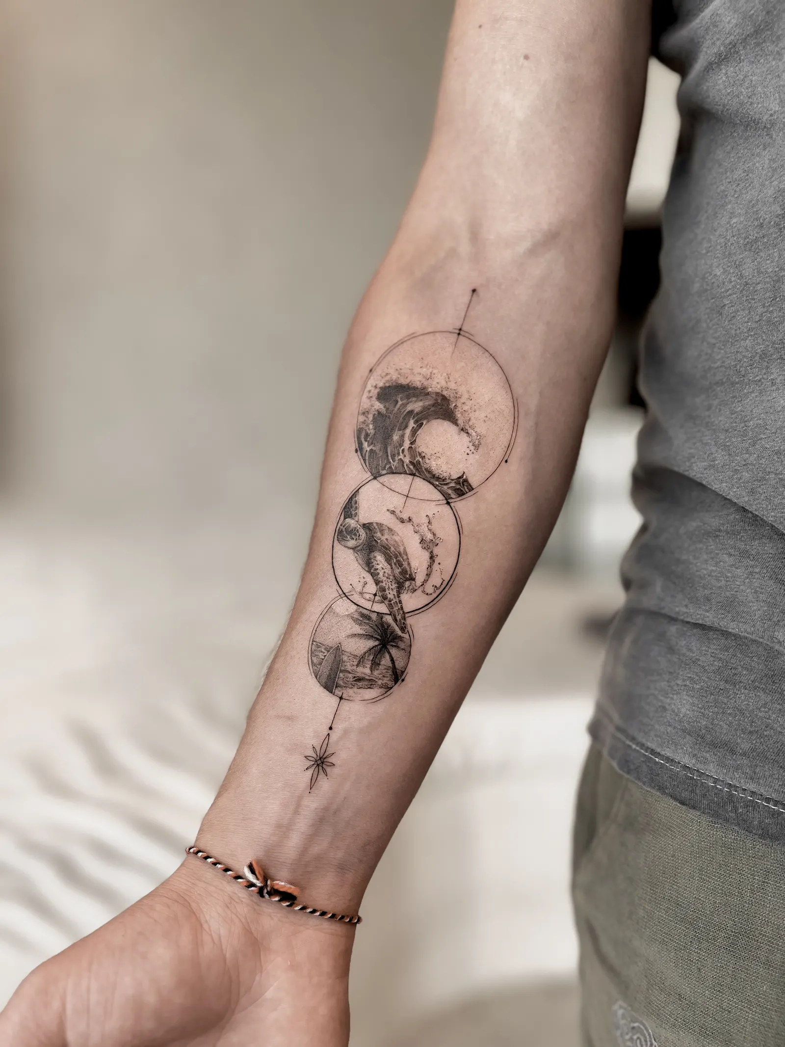 Three linked circles holding a wave, a sea turtle and palm trees on a forearm.