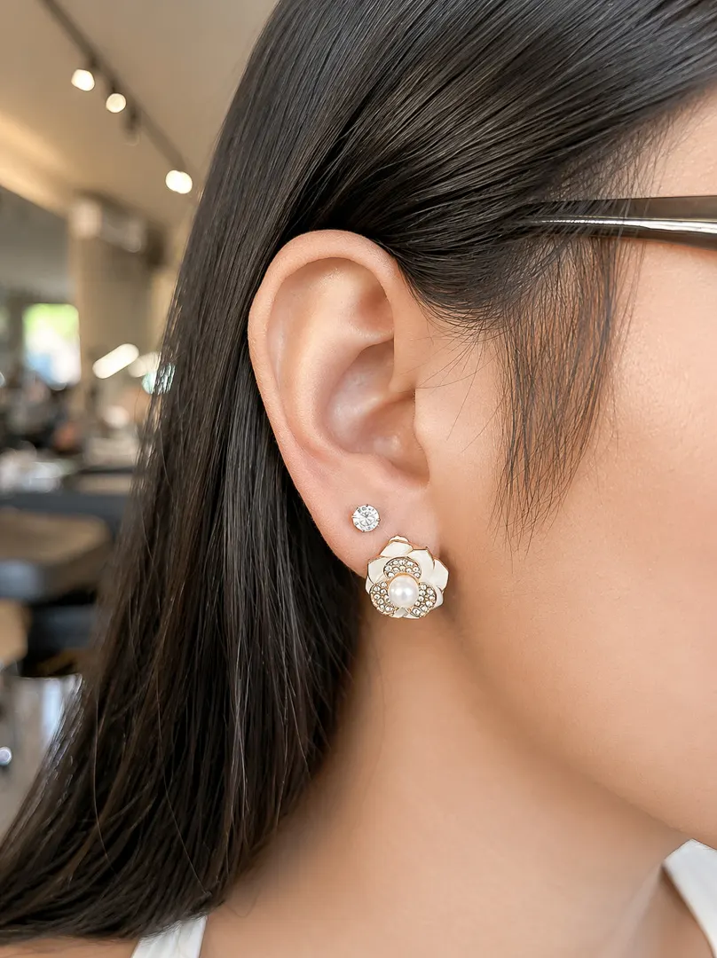 Close-up of an ear with a crystal stud and a flower-shaped earring.