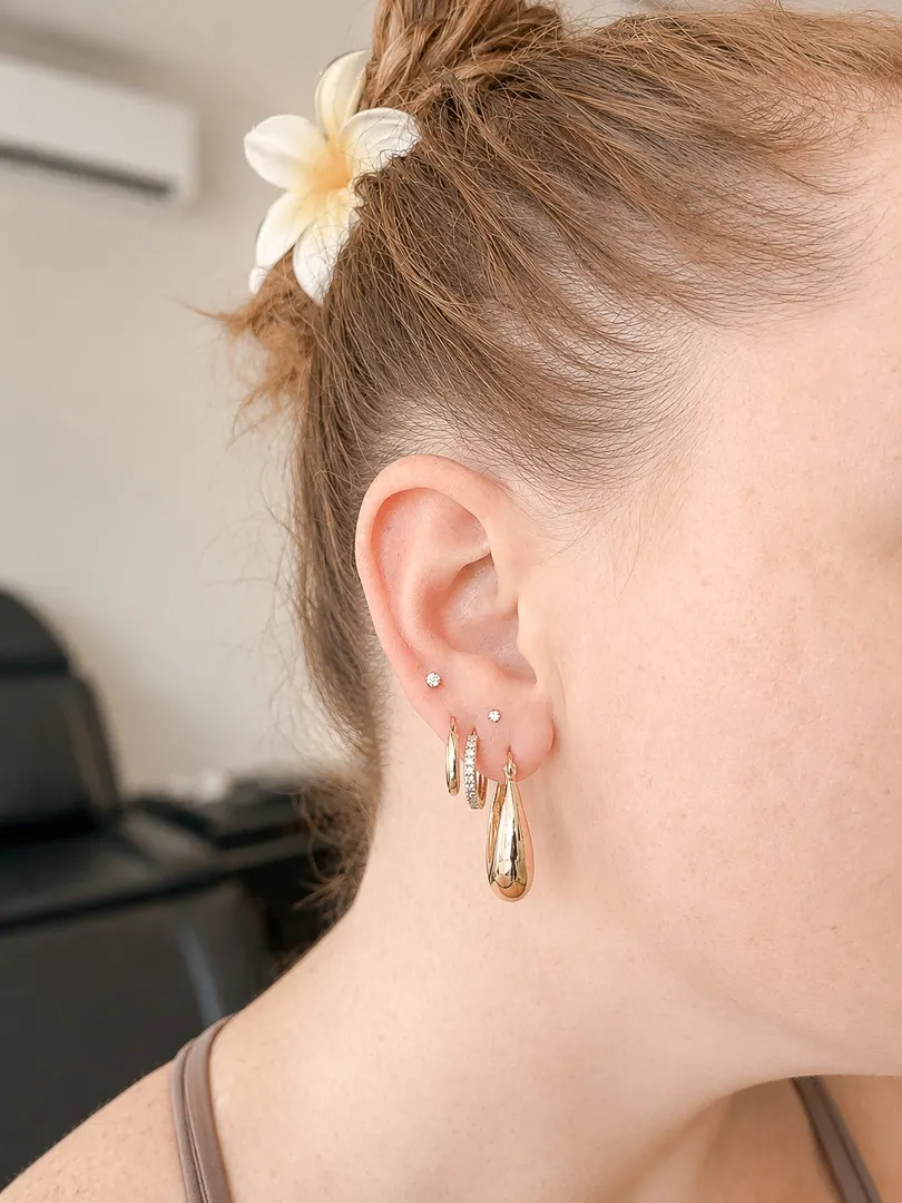 Close-up of an ear with gold hoop earrings and small stud piercings.